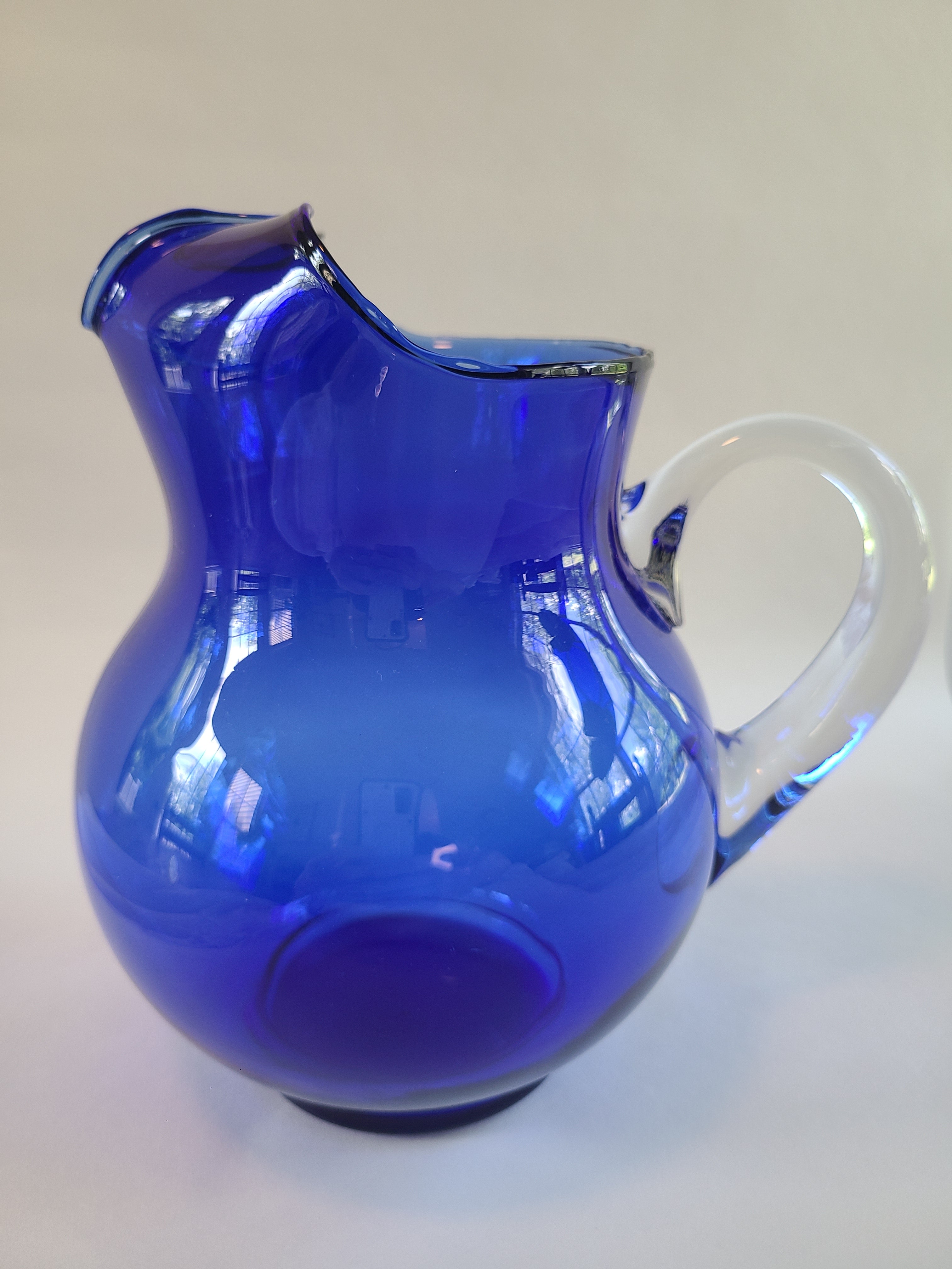 A vintage cobalt blue glass pitcher with a clear glass handle showing reflections.