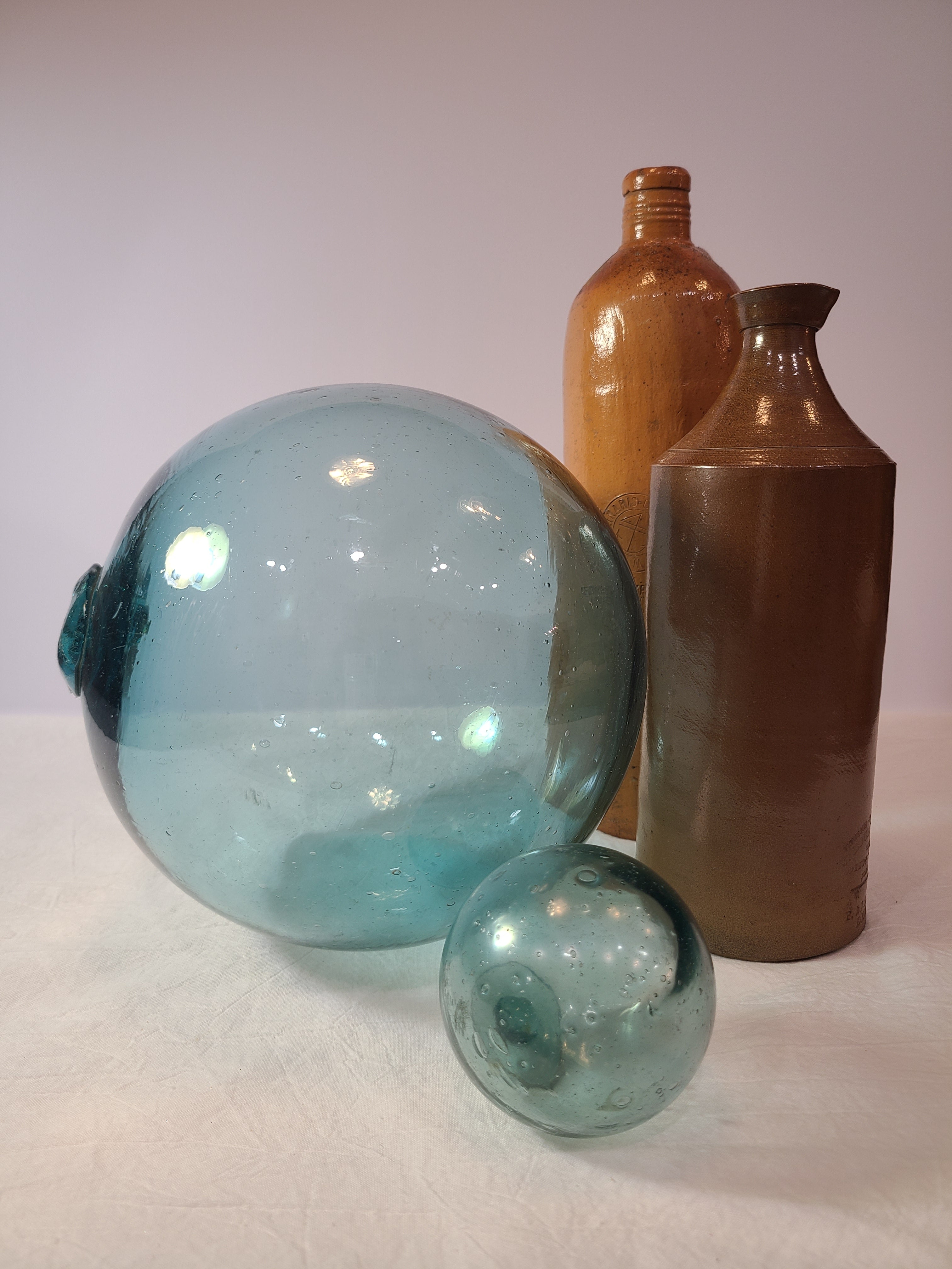 Authentic Glass Fishing Float 7" diameter in classic blue-green shown with smaller glass fishing float and stoneware bottles.