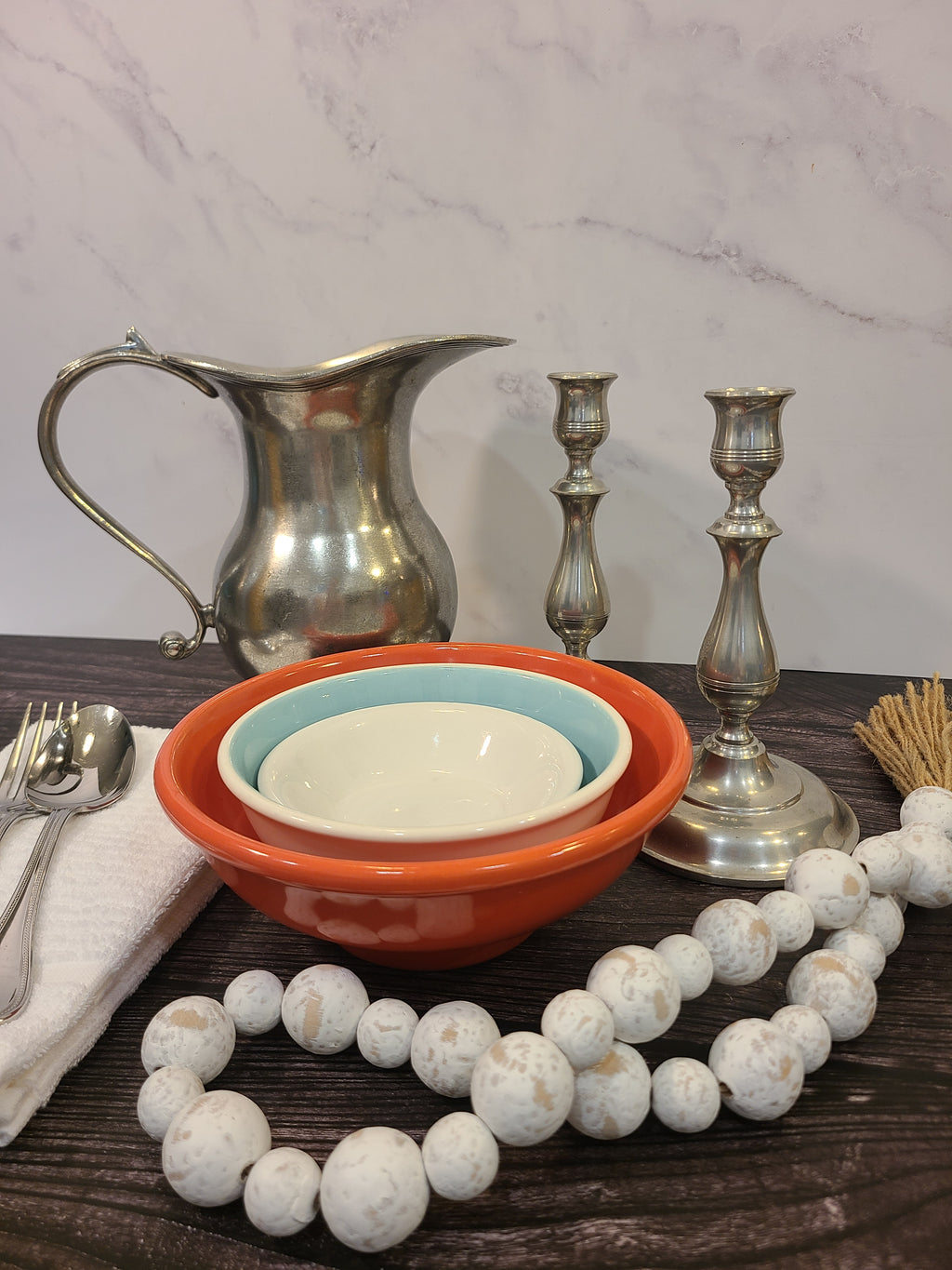 Vintage pewter water pitcher with S-scroll handle and stepped tiered foot, European artisan design circa late 1970s–1980s, 8.25 inches tall shown with bowls, candle sticks, wood beads.