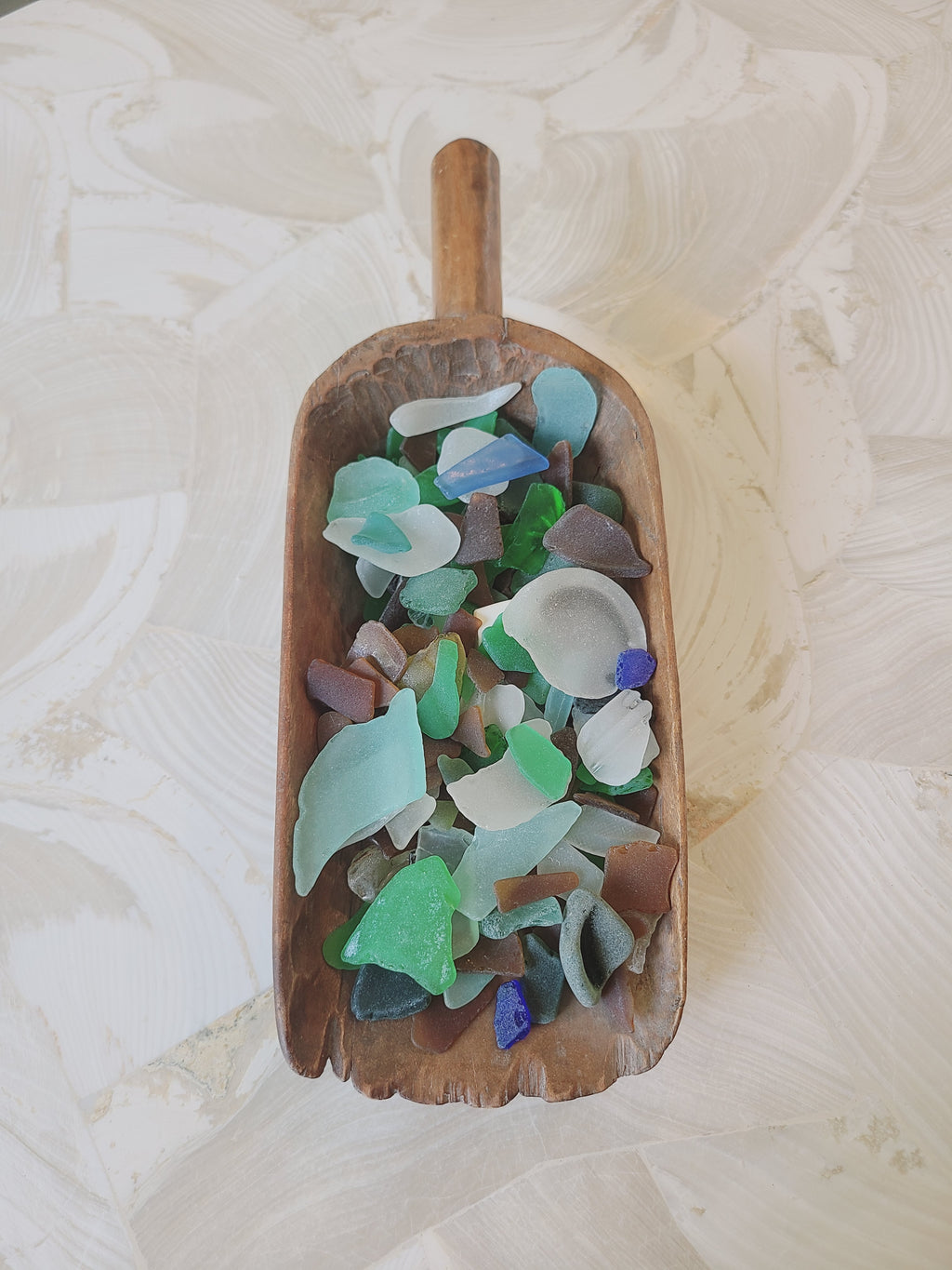 Antique hand-carved hardwood grain scoop filled with colorful sea glass — coastal cottage decor styling idea