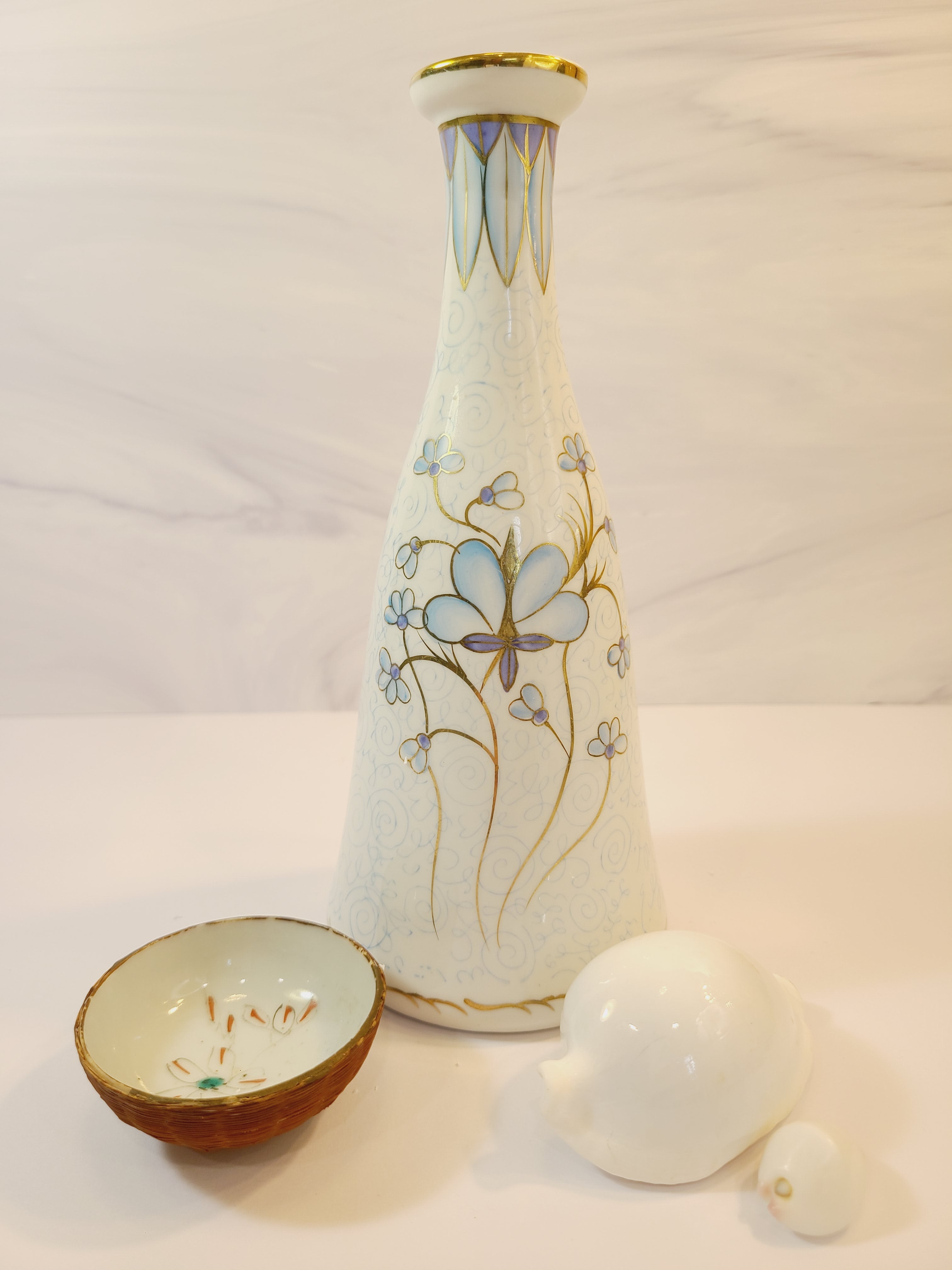 Andrea by Sadek vintage white porcelain vase made in Japan hand-painted with light blue floral motifs, gold accents, and a blue-and-gold patterned band at the neck displayed with white shells and small porcelain dish.