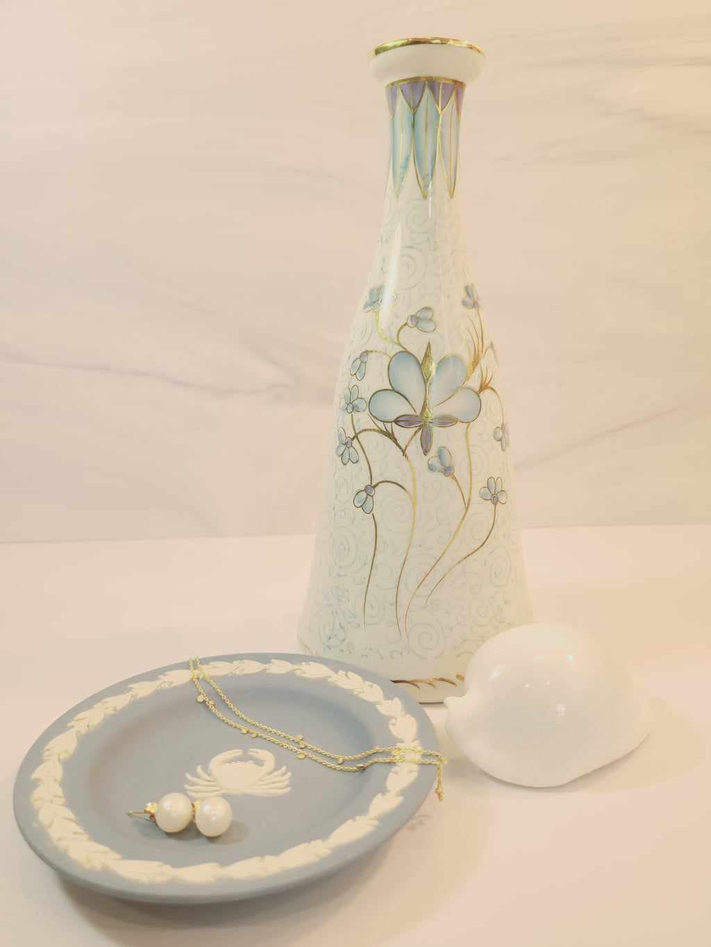 Andrea by Sadek vintage white porcelain vase made in Japan hand-painted with light blue floral motifs, gold accents, and a blue-and-gold patterned band at the neck displayed with white shell and dish holding jewelry.