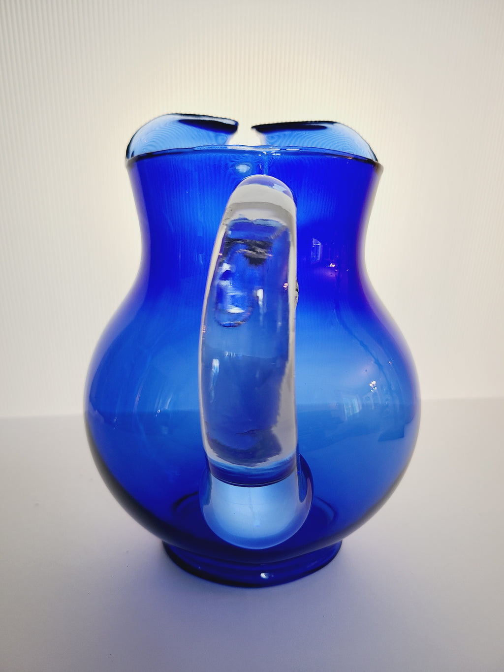 A vintage cobalt blue glass pitcher with a clear glass handle, photographed to show the handle.
