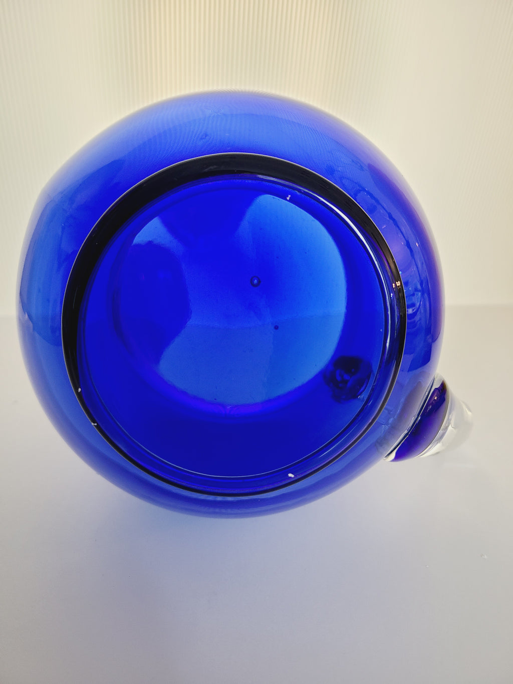Bottom of a vintage cobalt blue glass pitcher with a clear glass handle.