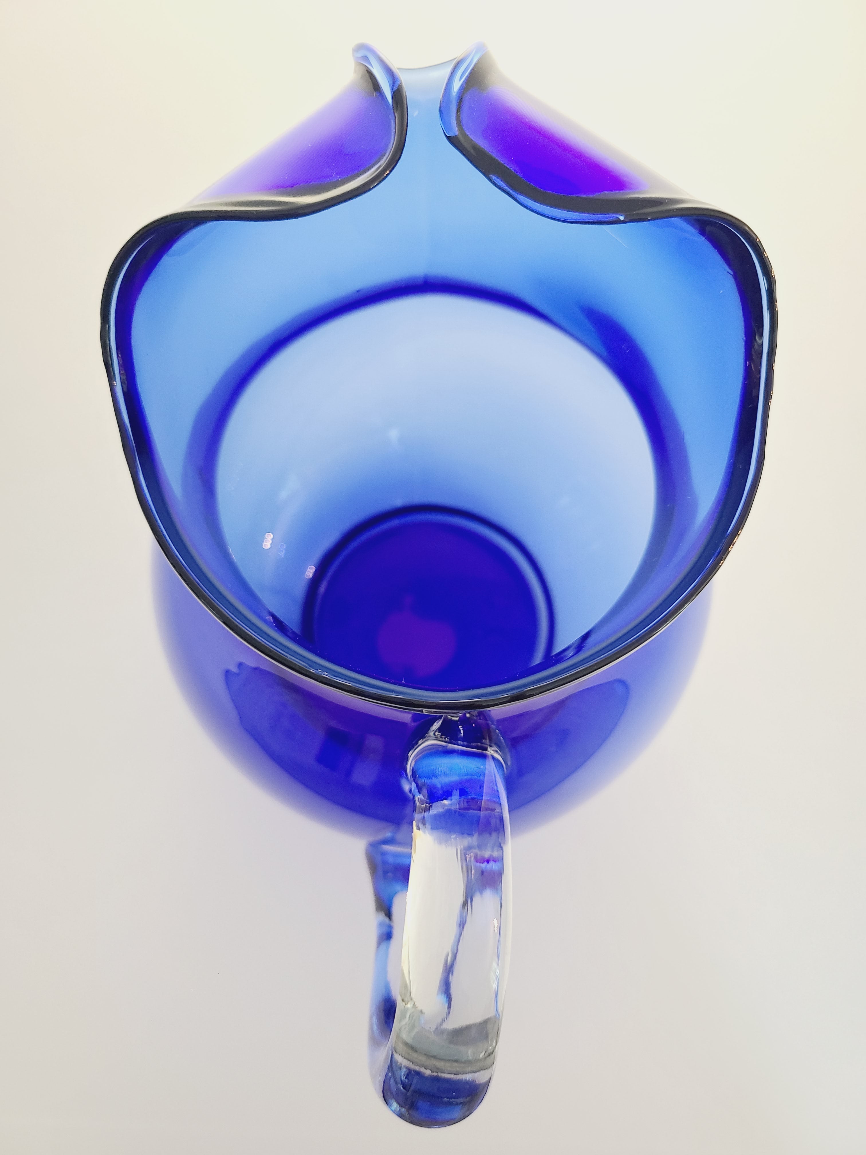 A vintage cobalt blue glass pitcher with a clear glass handle photographed with a top down view.