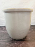 Vintage Handmade White Glazed Crock sitting on a dark wood surface against a white textured wall.