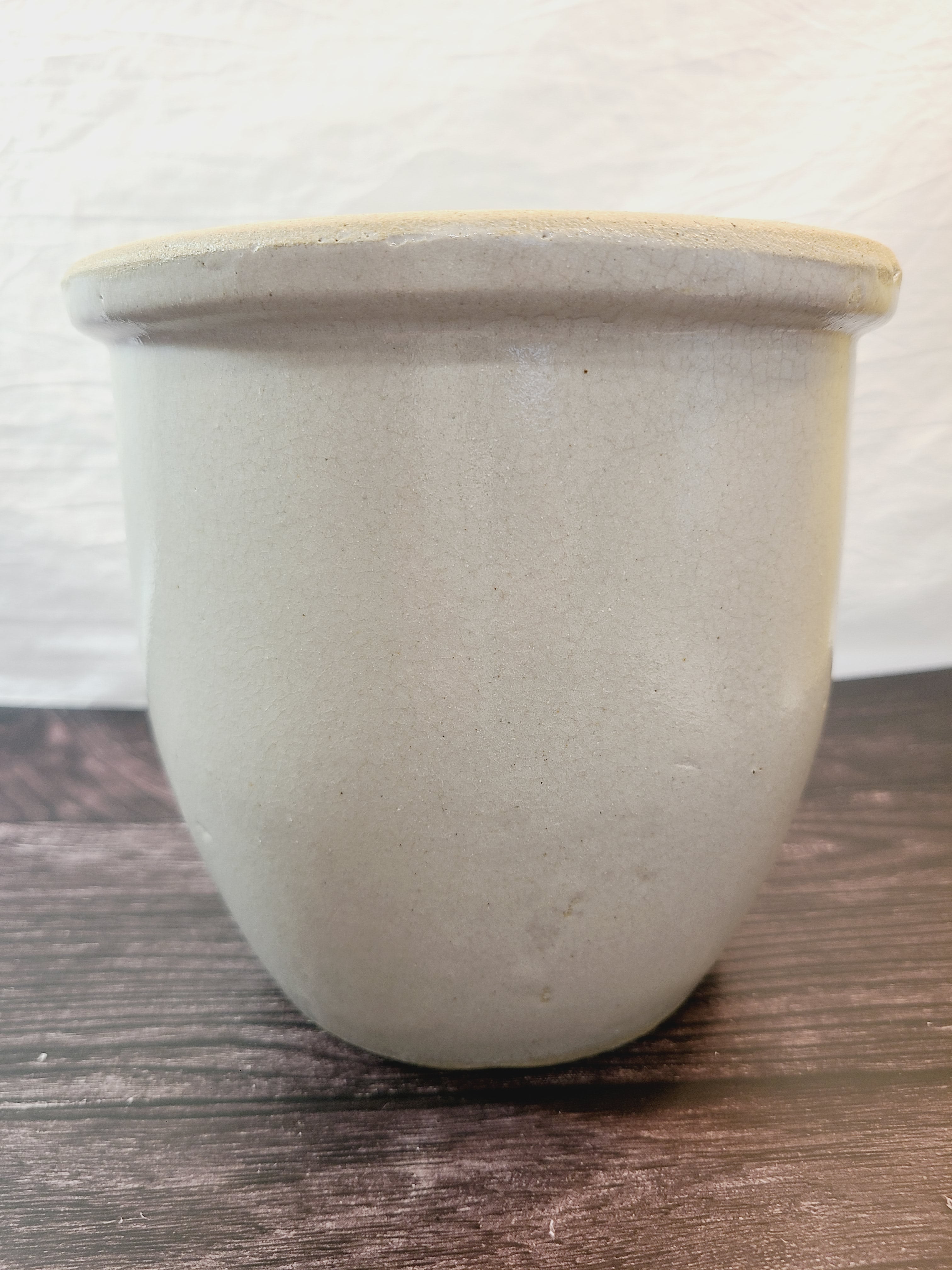 Vintage Handmade White Glazed Crock sitting on a dark wood surface against a white textured wall.