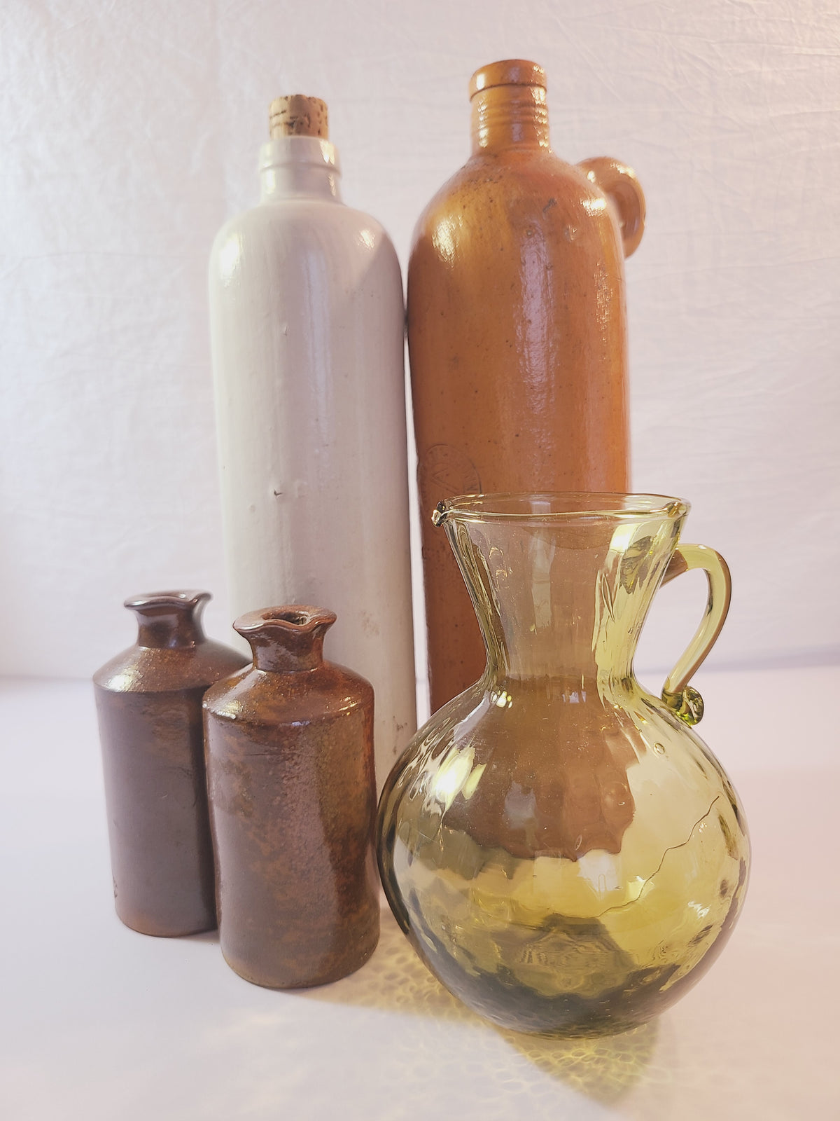 Petite olive green handblown optic glass pitcher displayed with stoneware bottles