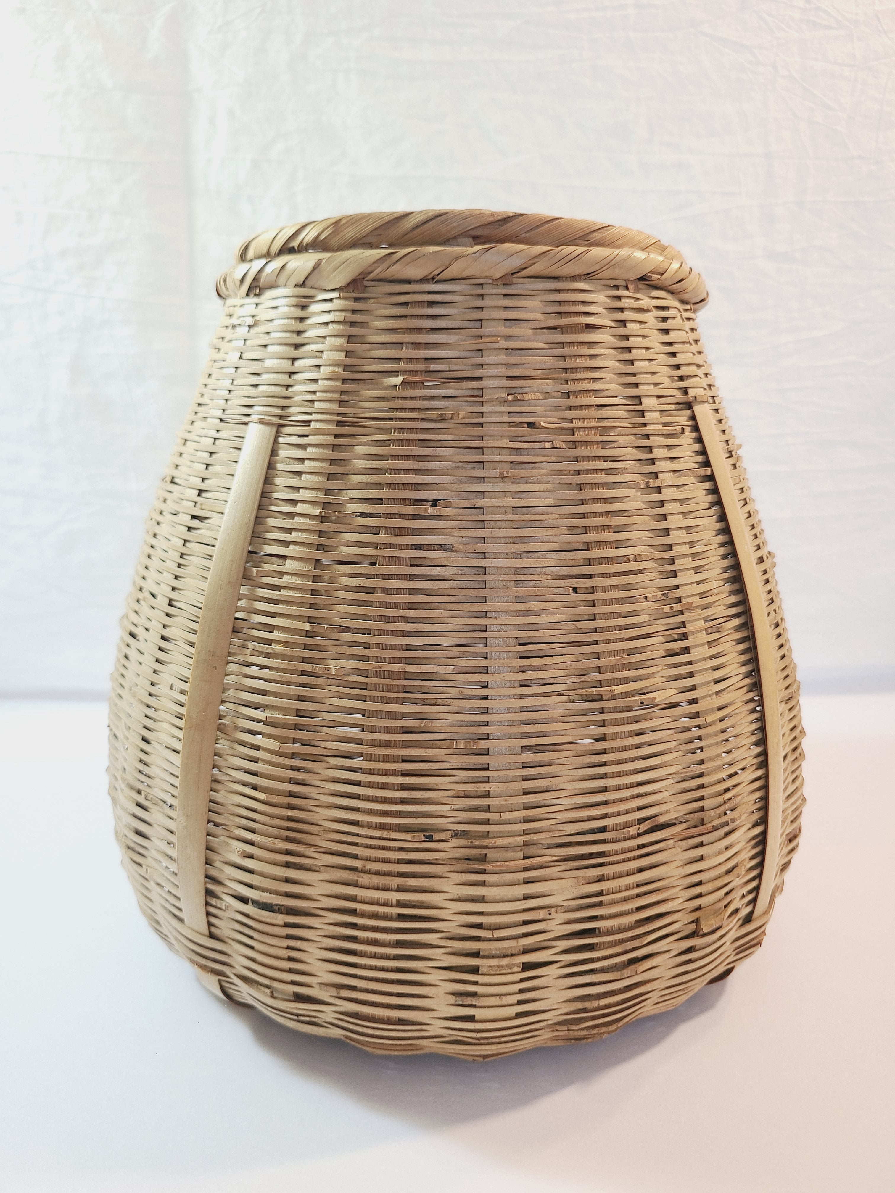 A natural woven wicker basket with a rounded, tapered shape ashown against a plain white background.