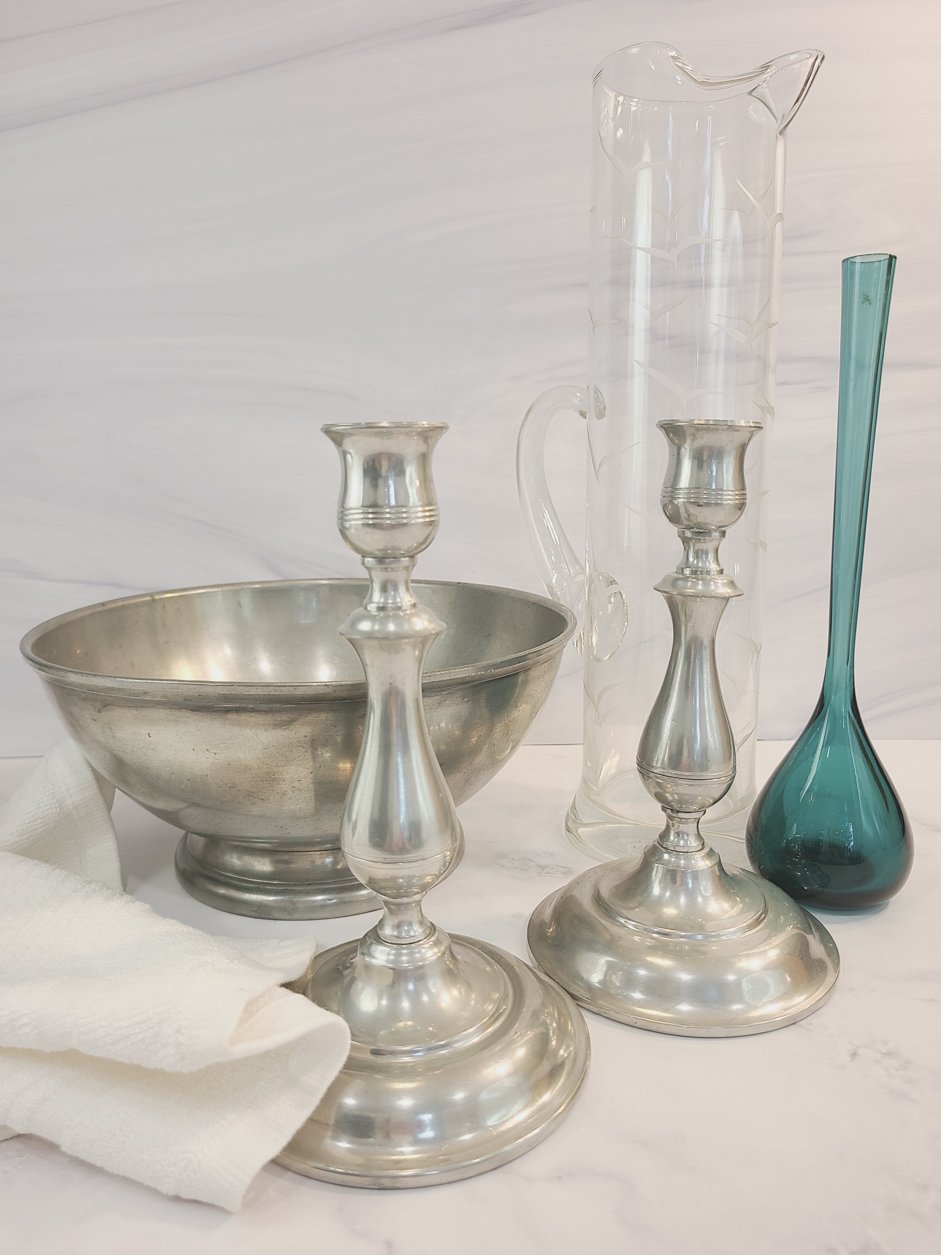 A translucent vintage teal glass vase made in Sweden displayed with pewter candle holders, pewter bowl, clear glass pitcher.