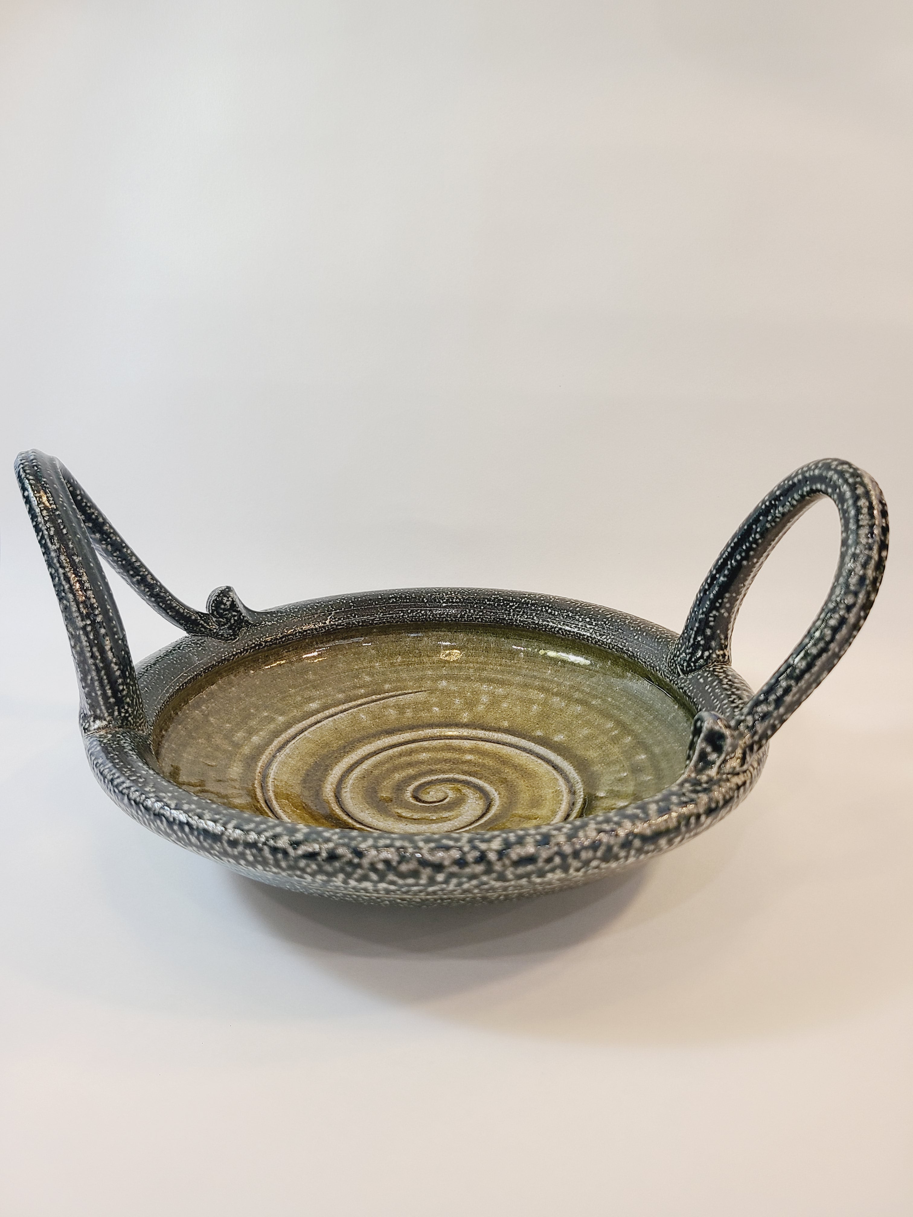 Jon Faulkner studio Pottery Bowl in shades of olive green and darkest blue or black on a white background.