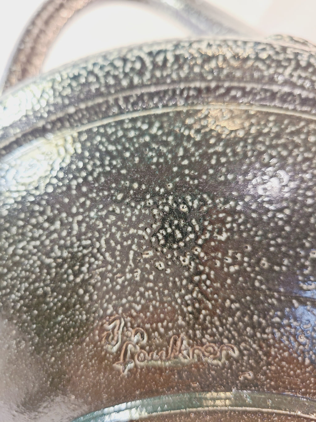 Close up of Jon Faulkner studio Pottery Bowl in shades of olive green and darkest blue or black showing signature. 