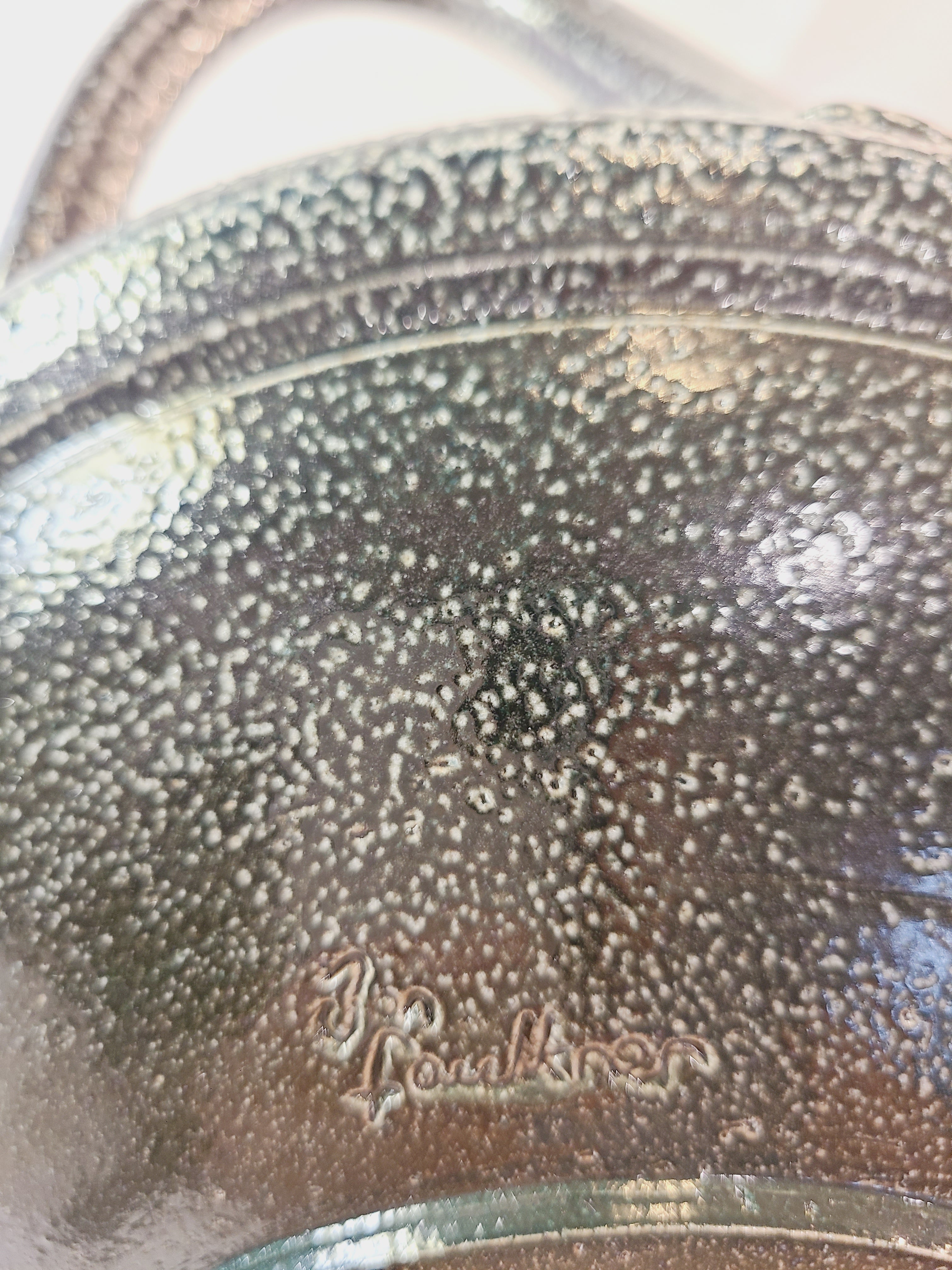 Close up of Jon Faulkner studio Pottery Bowl in shades of olive green and darkest blue or black showing signature. 