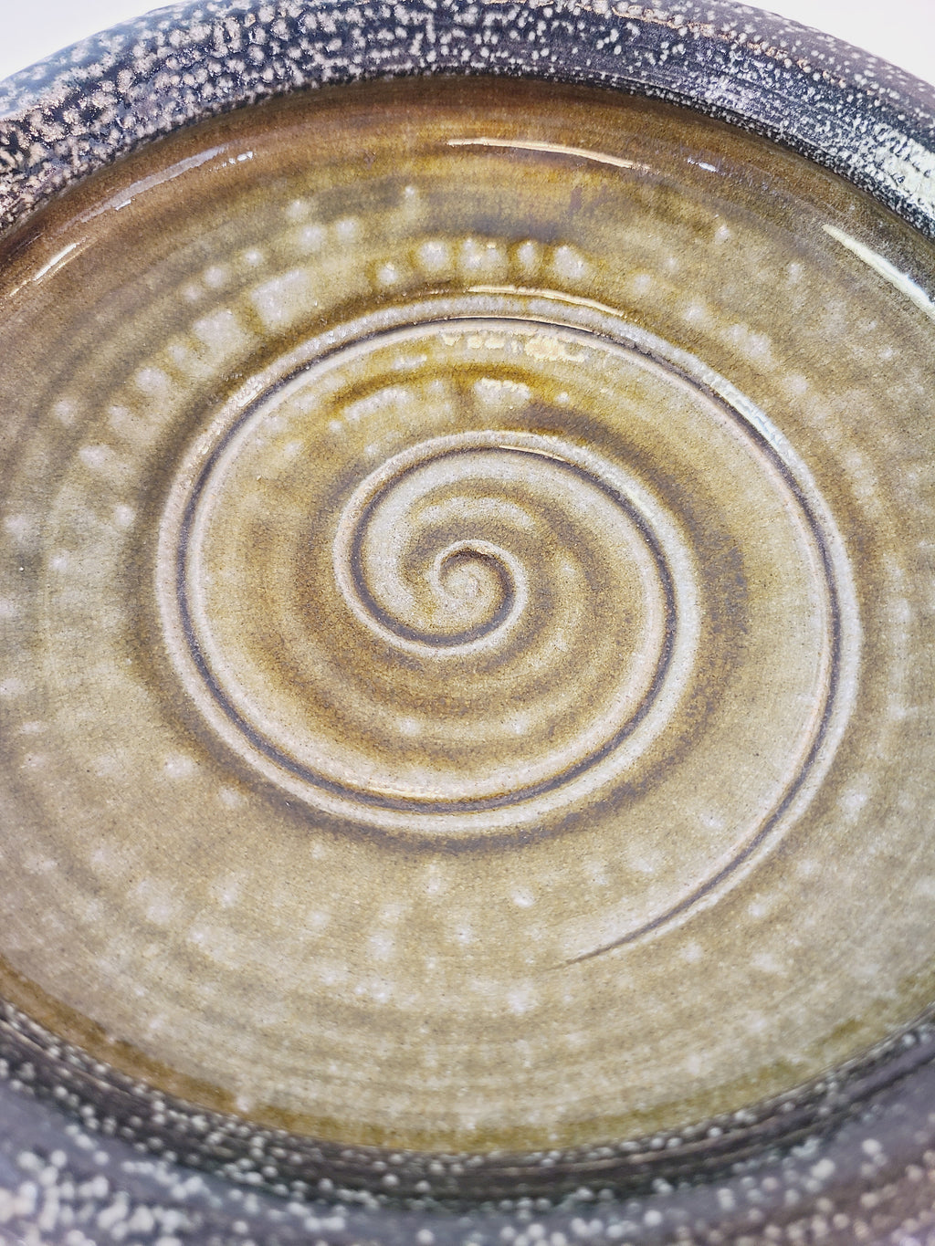 Close up of spiral design on Jon Faulkner studio Pottery Bowl in shades of olive green and darkest blue or black.