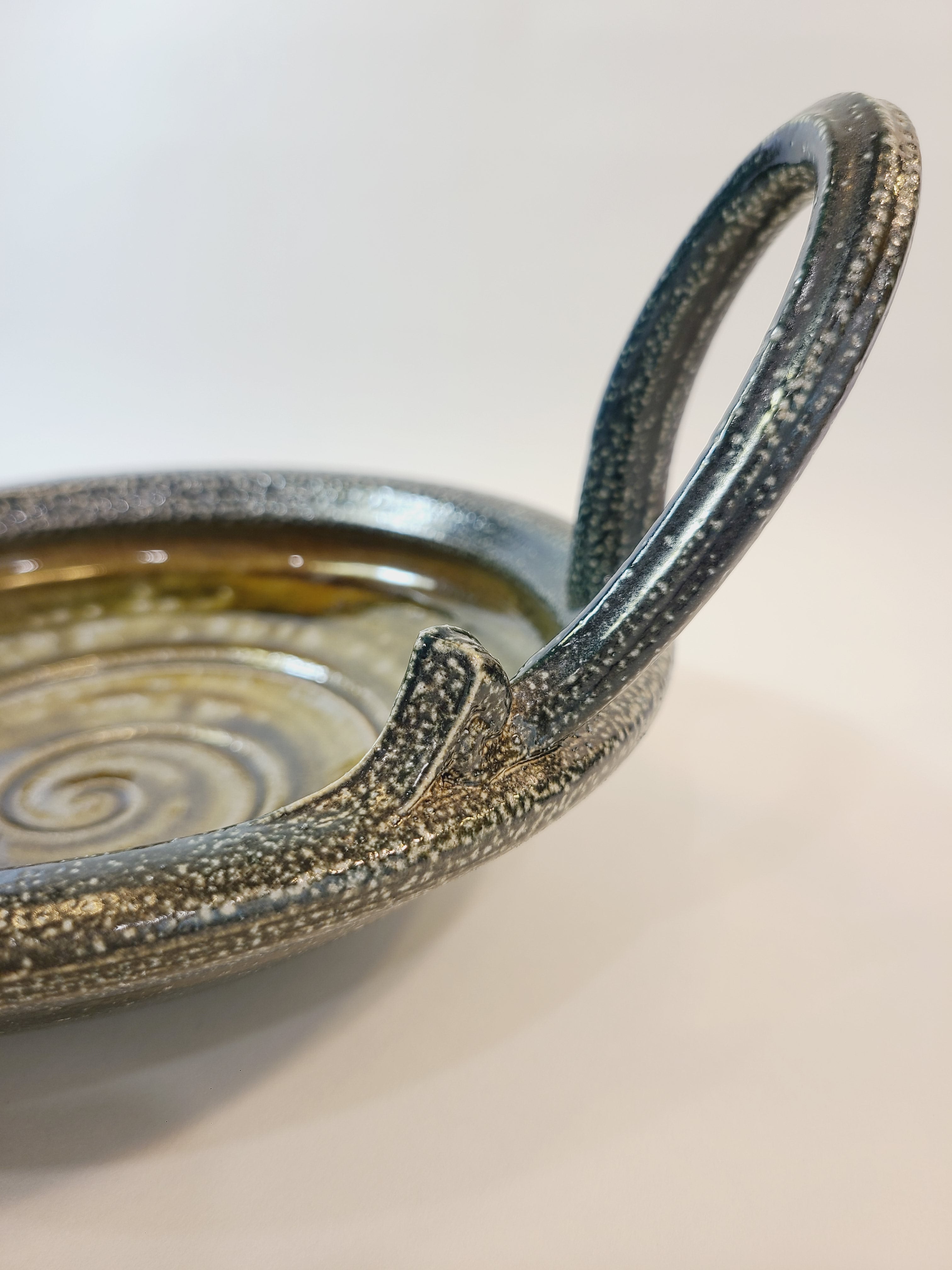Close up of handle of Jon Faulkner studio Pottery Bowl in shades of olive green and darkest blue or black.