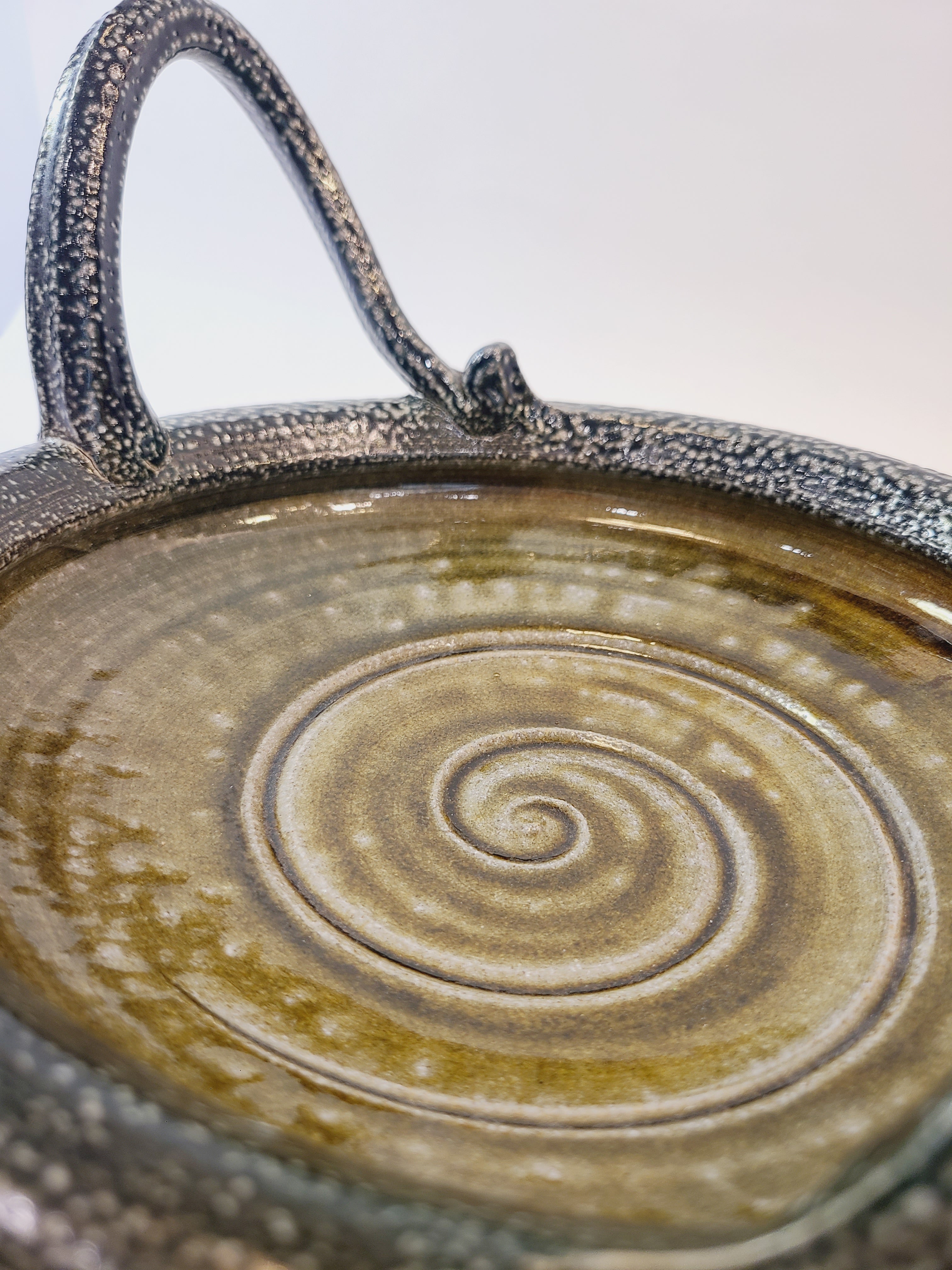 Close of of middle of Jon Faulkner studio Pottery Bowl in shades of olive green and darkest blue or black.