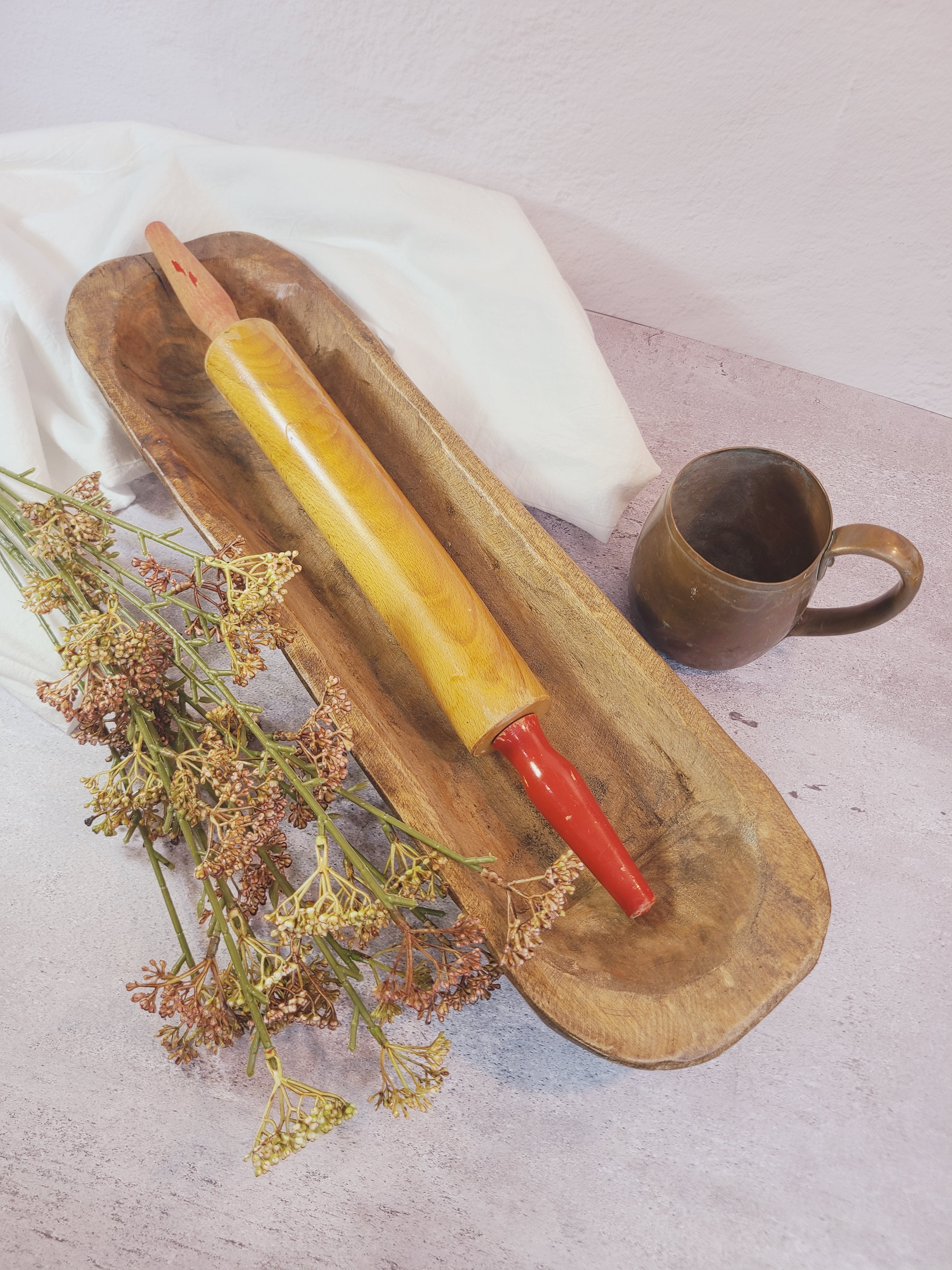 Oblong vintage Handcrafted Wood Dough Bowl shown with wooden rolling pin, dried flowers, copper mug.