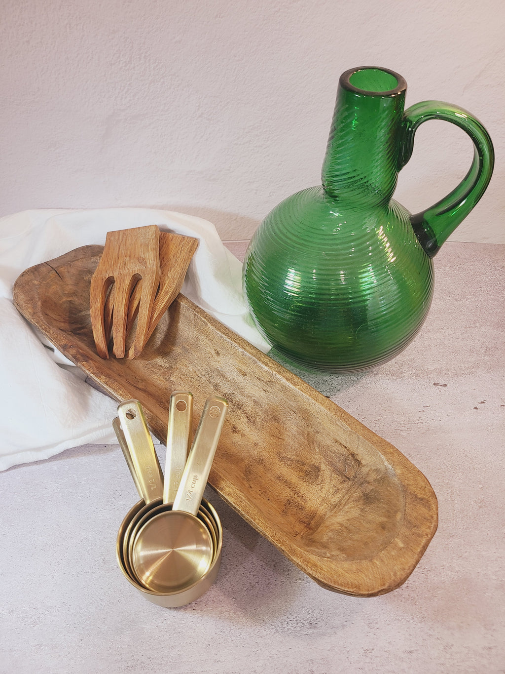 Oblong vintage Handcrafted Wood Dough Bowl shown with green bottle, brass measuring cuts, wooden salad scoops.