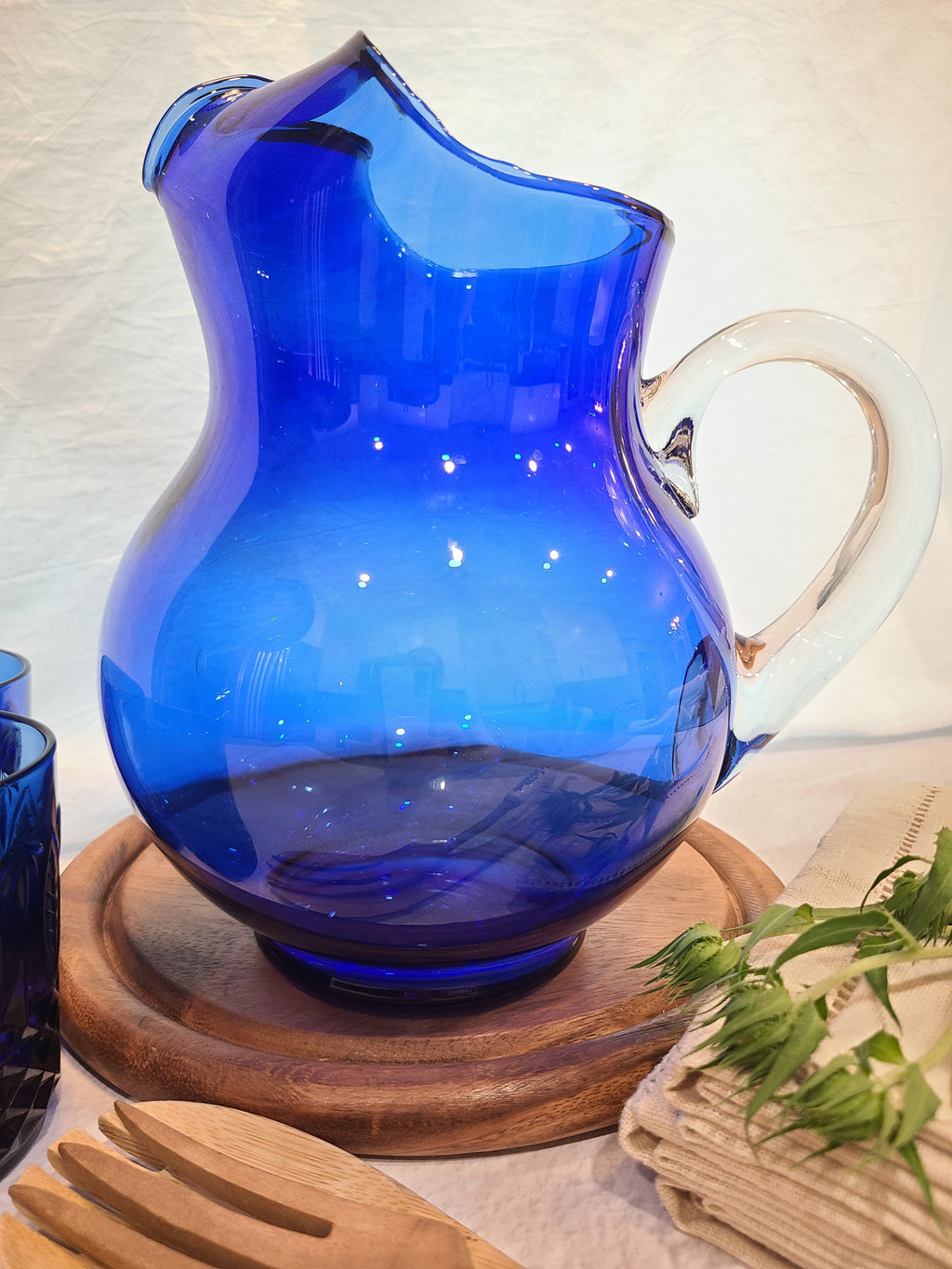 A vintage cobalt blue glass pitcher with a clear glass handle shown in a table setting.