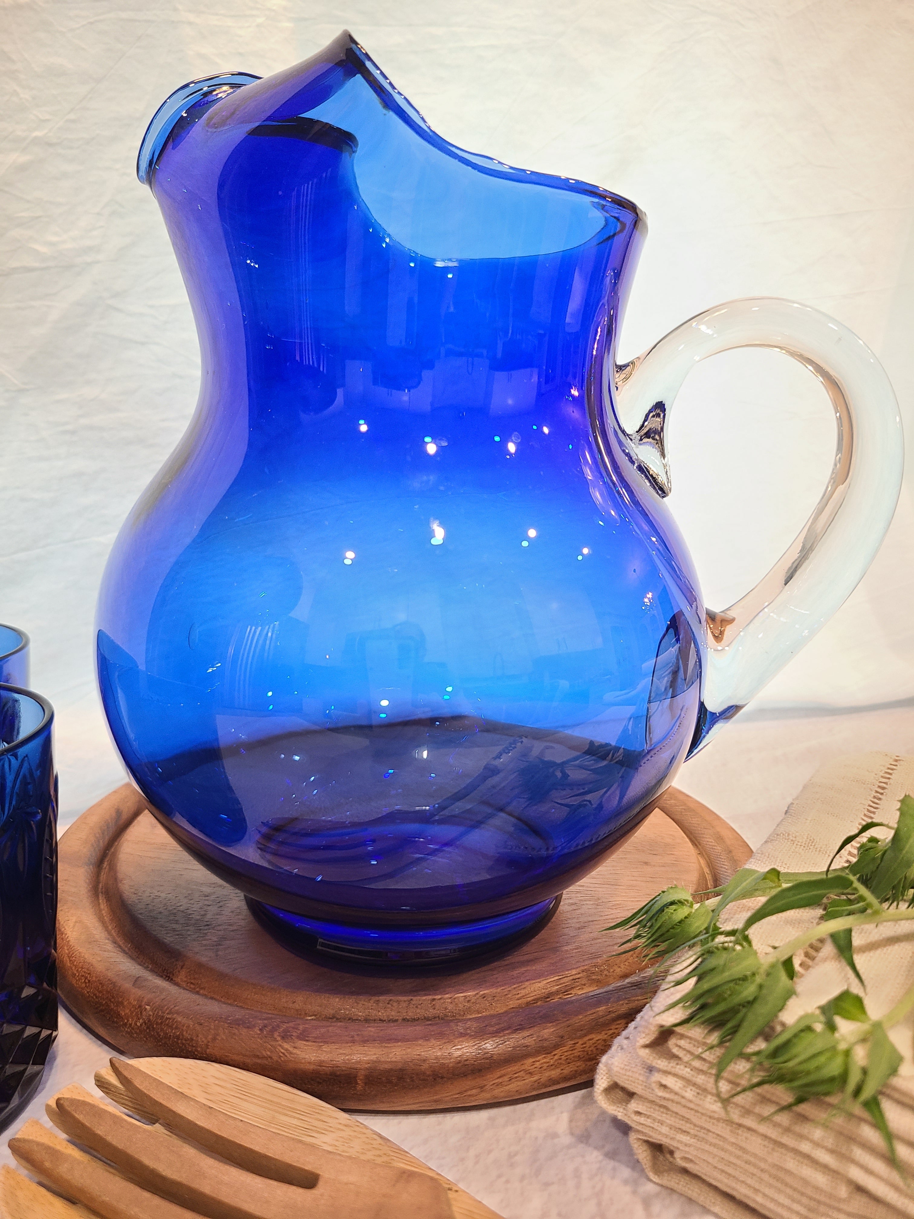 A vintage cobalt blue glass pitcher with a clear glass handle shown in a table setting.