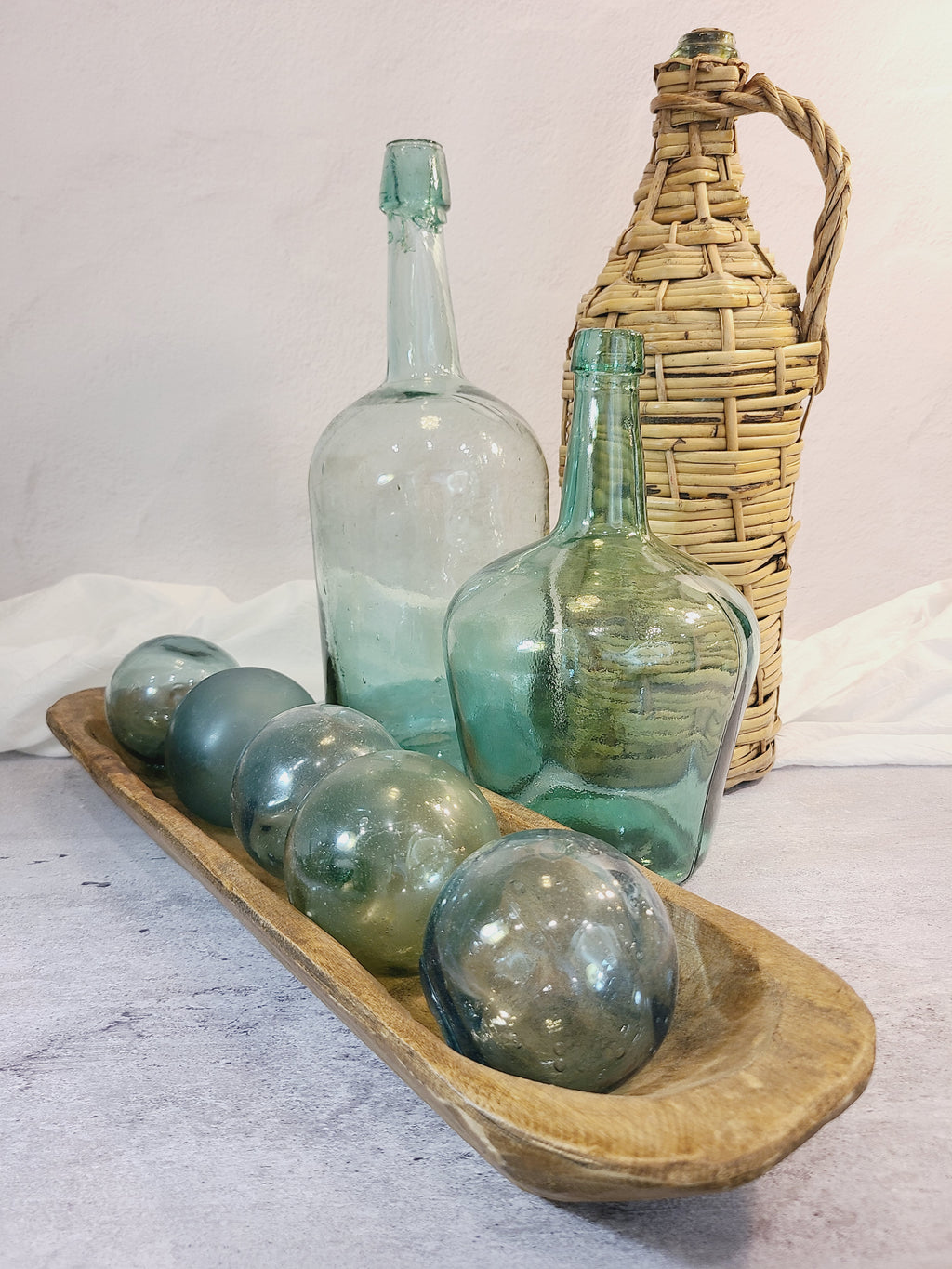 Vintage Green Glass Demijohn 10" shown with another demijohn in wicker wrapping and glass fishing floats in wood bowl