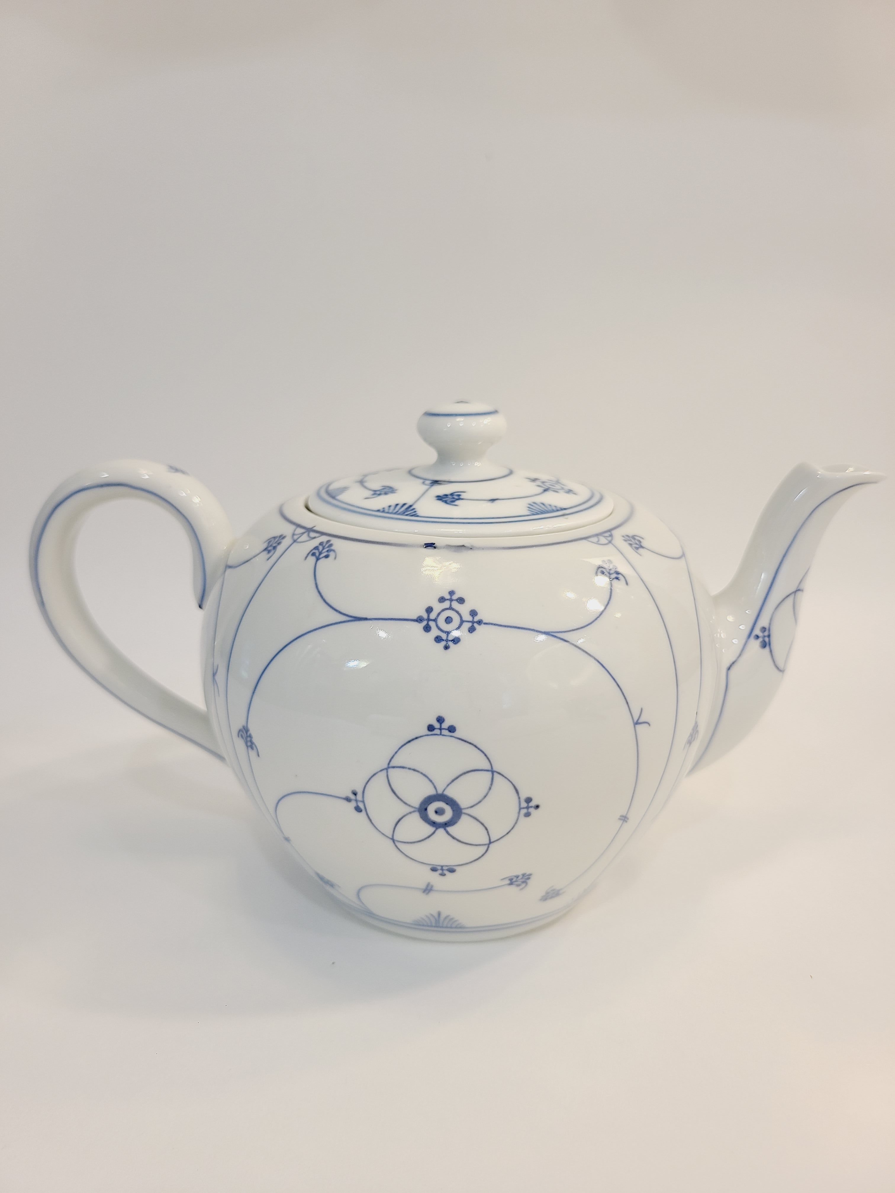 A vintage white ceramic teapot with a blue floral pattern shown from the side.