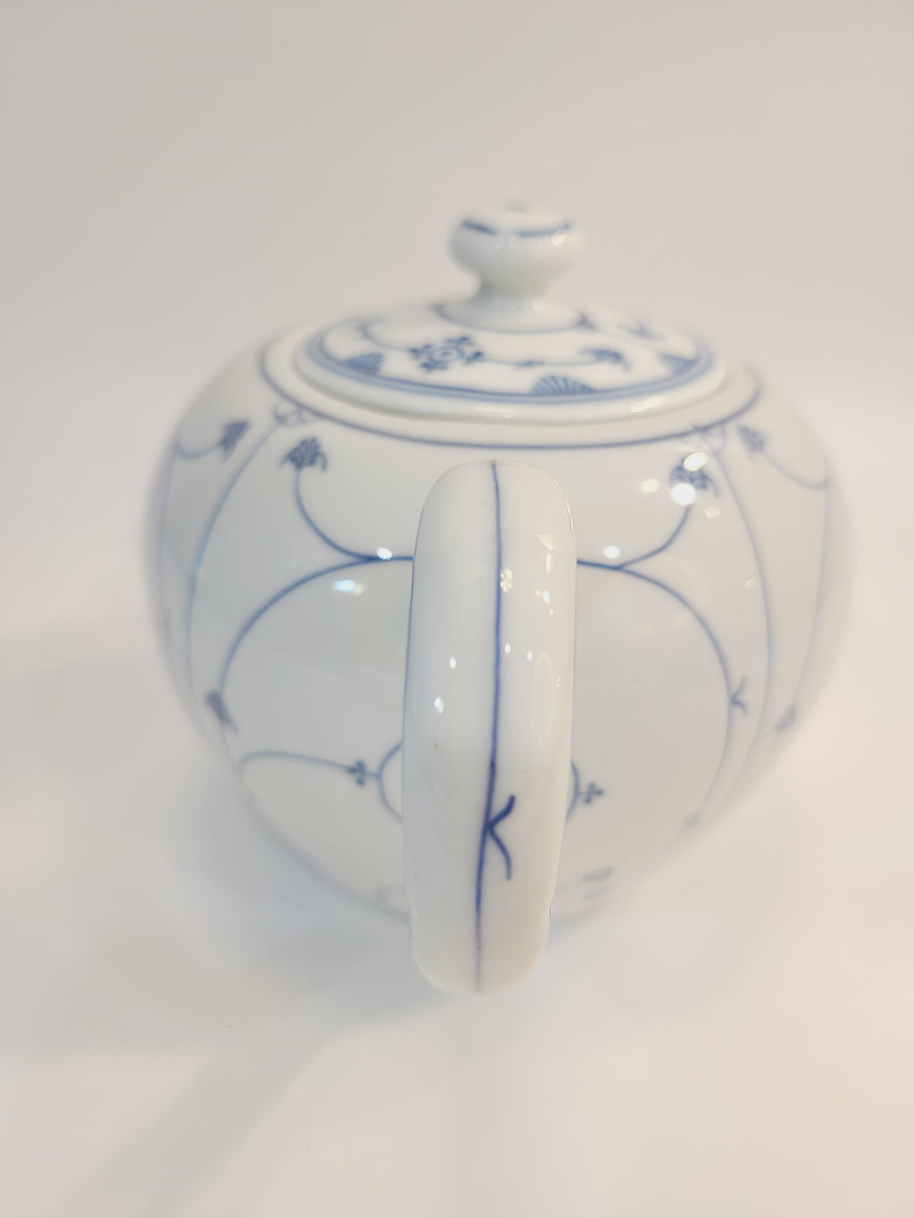 A vintage white ceramic teapot with a blue floral vine pattern showing the handle.