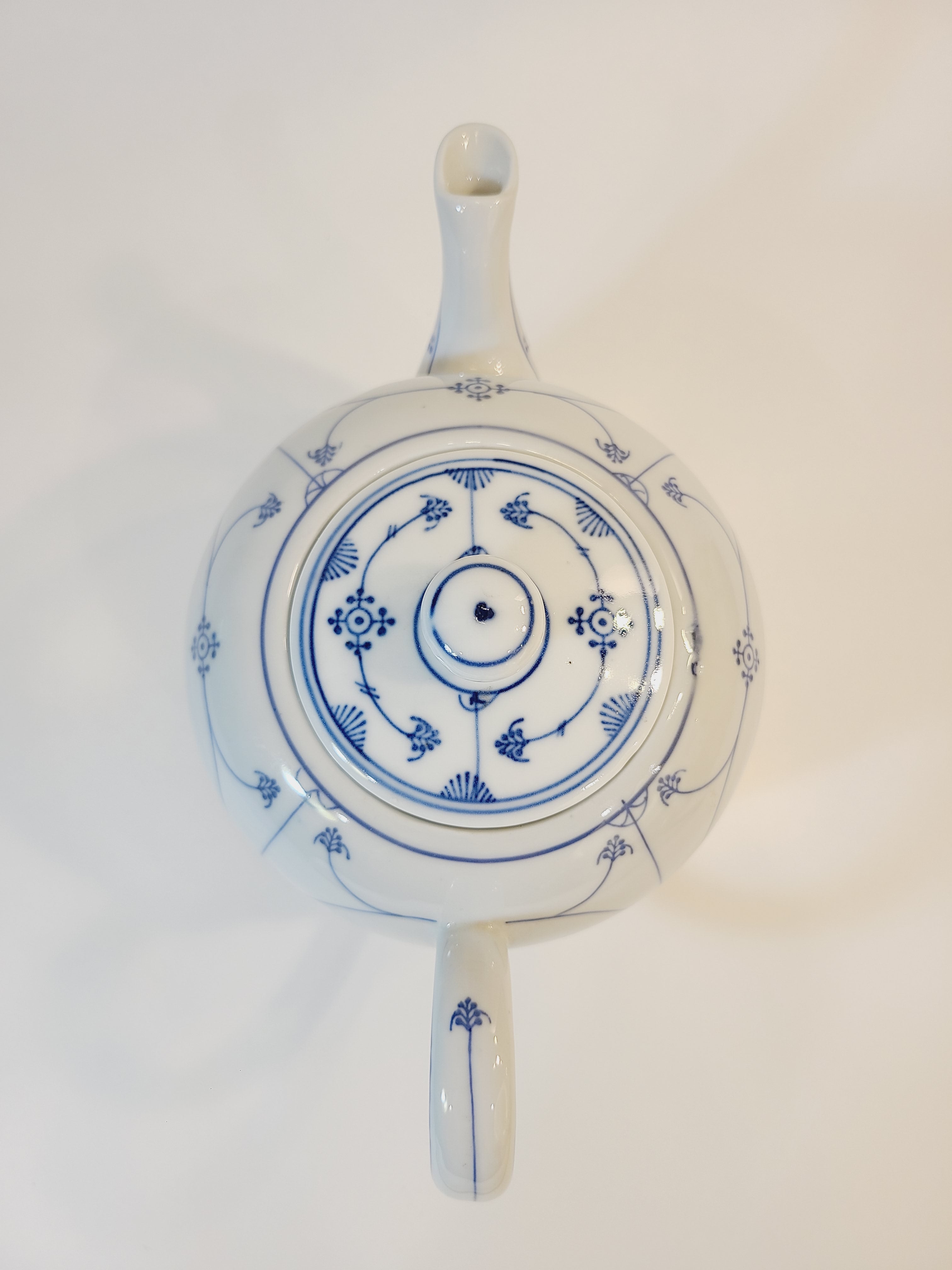 A vintage white ceramic teapot viewed from the top, featuring blue floral design.