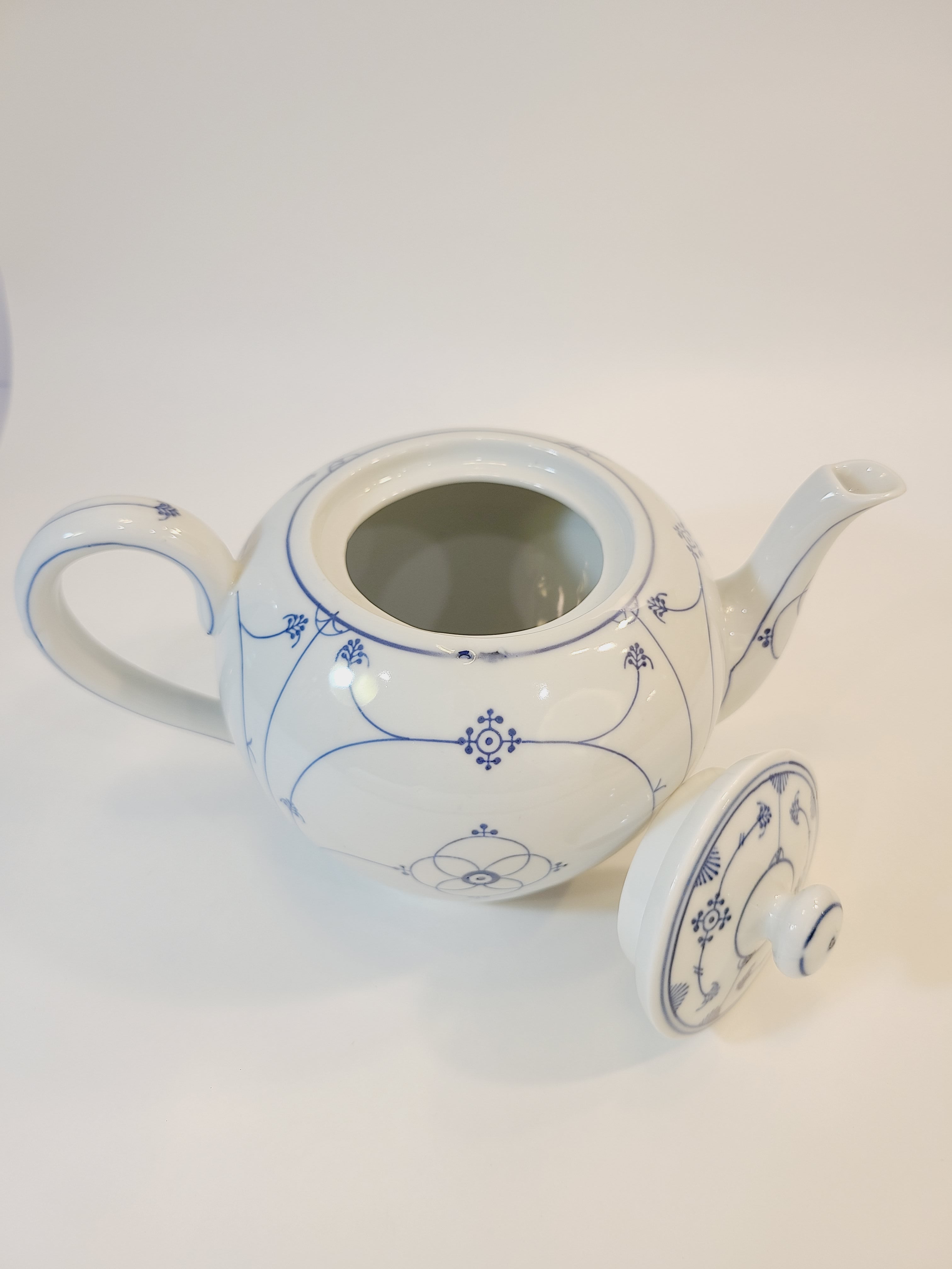 A vintage white ceramic teapot with blue floral pattern shown with lid off.