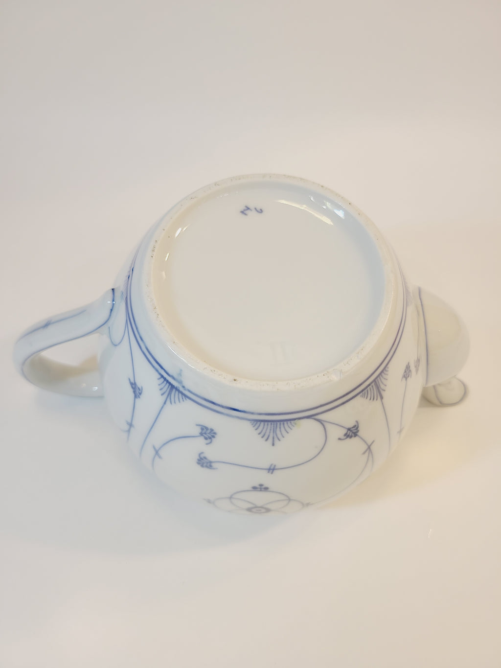 A vintage white ceramic teapot with blue floral patterns, photographed from the bottom.