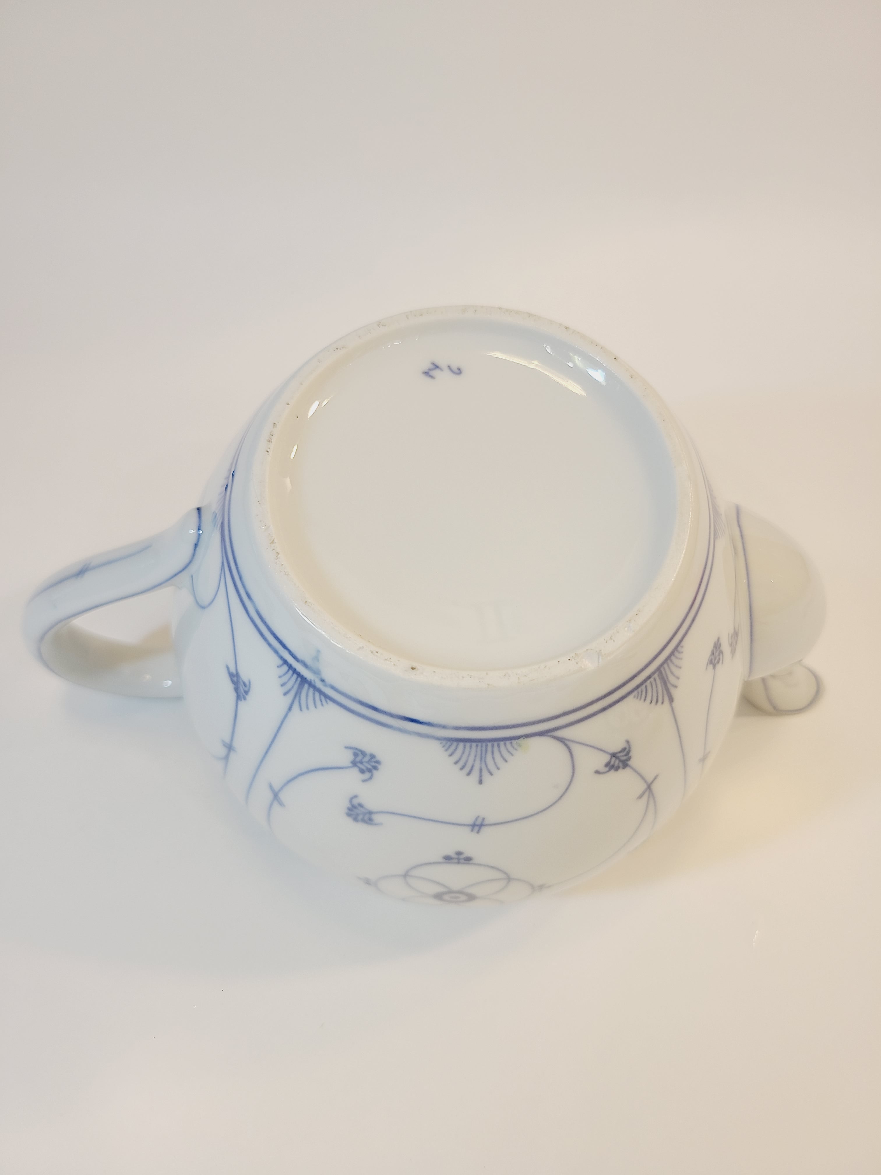 A vintage white ceramic teapot with blue floral patterns, photographed from the bottom.