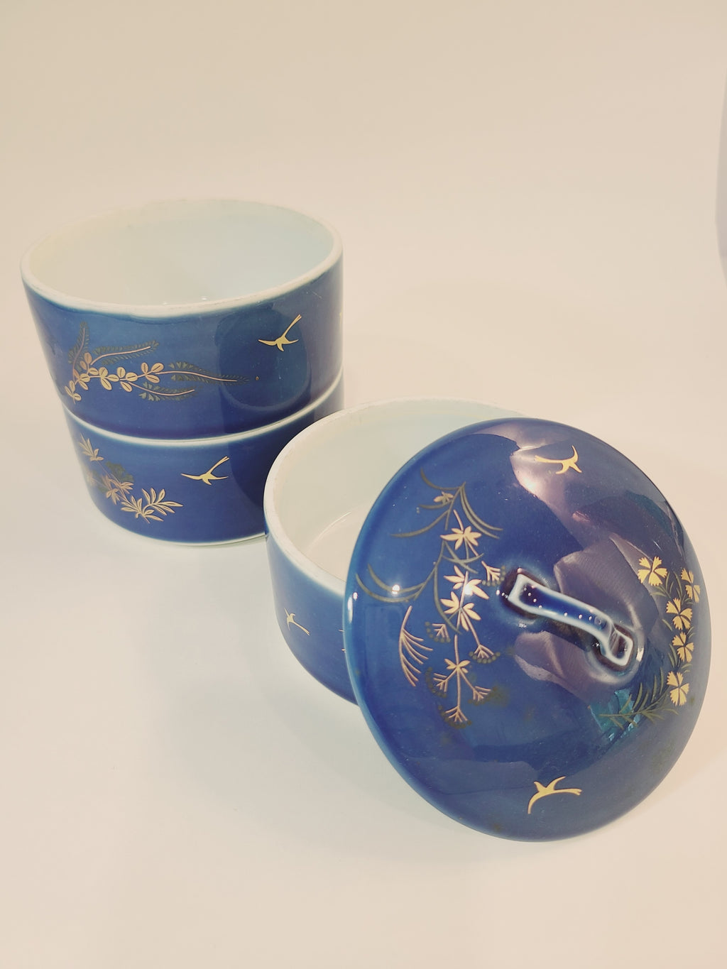 Vintage Fukagawa Seiji 3-Tier Stacking Bowl Set with Lid in lapis blue with gold accents with lid in foreground.