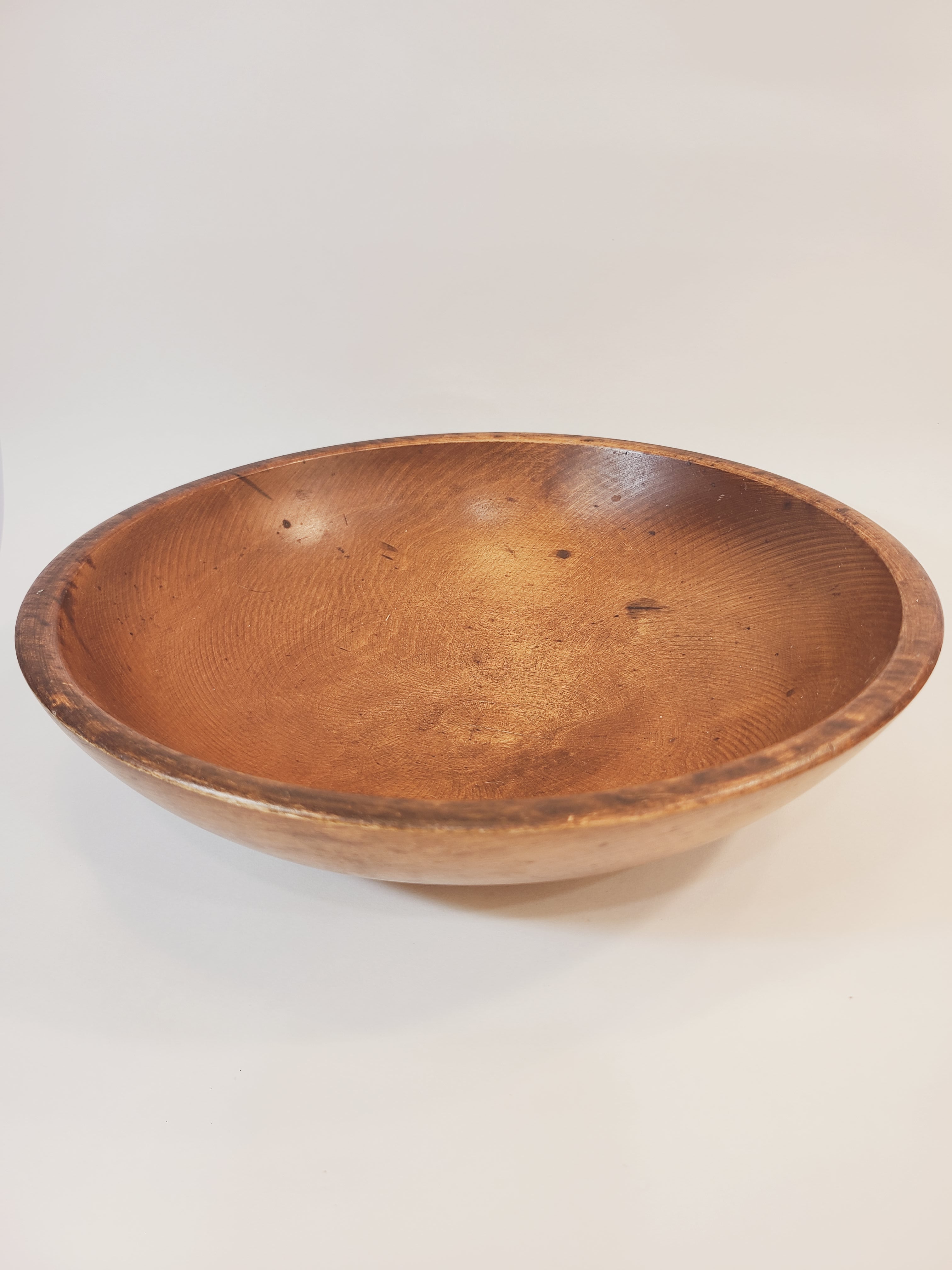 A large, vintage, round wooden bowl with a smooth, polished rim, shown against a plain off-white background.