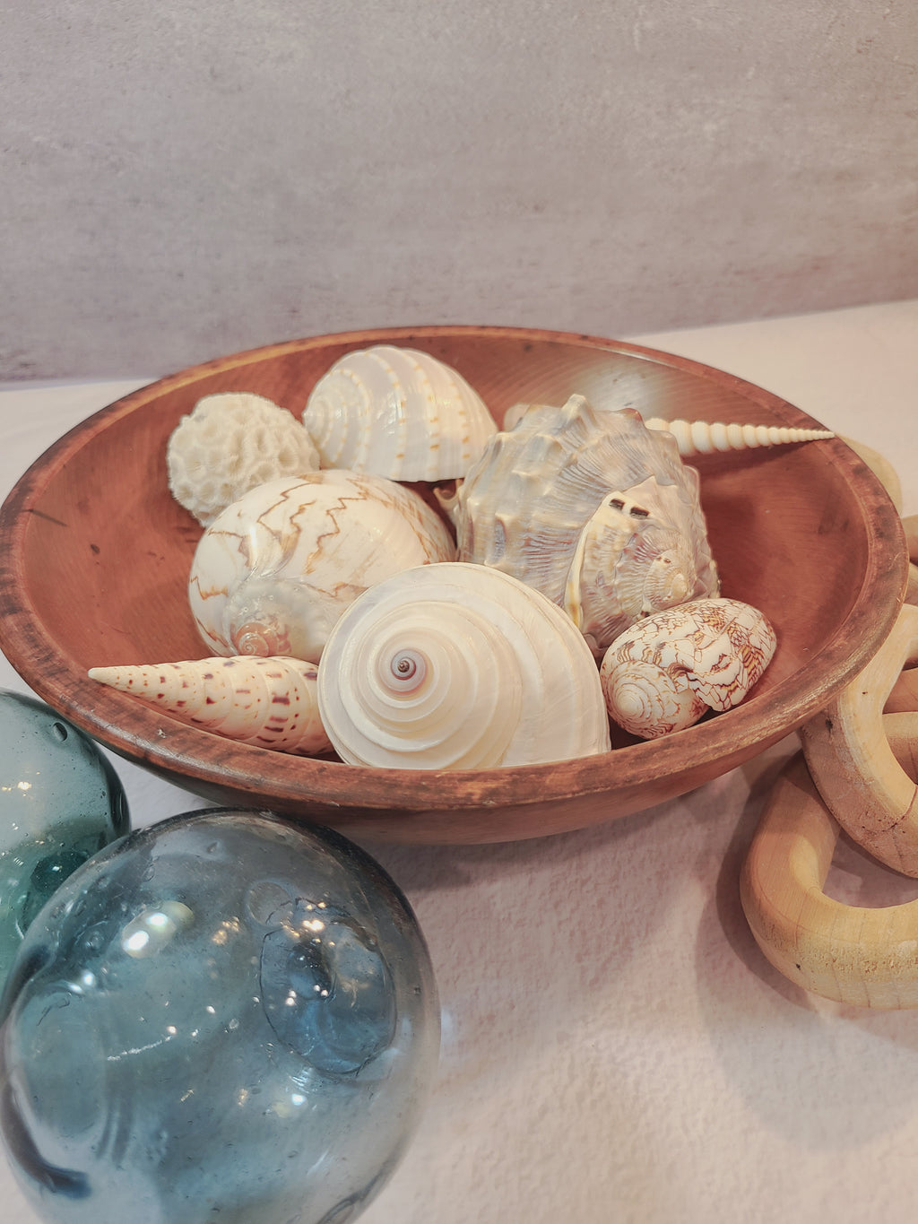 A collection of natural seashells inside a vintage round wooden bowl.