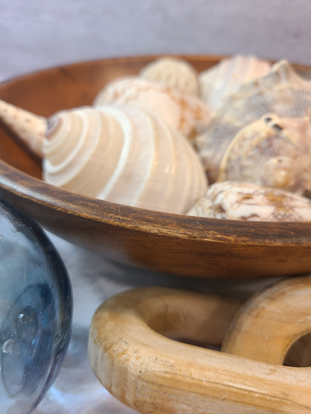 A close-up of a vintage wooden bowl filled with assorted seashells.