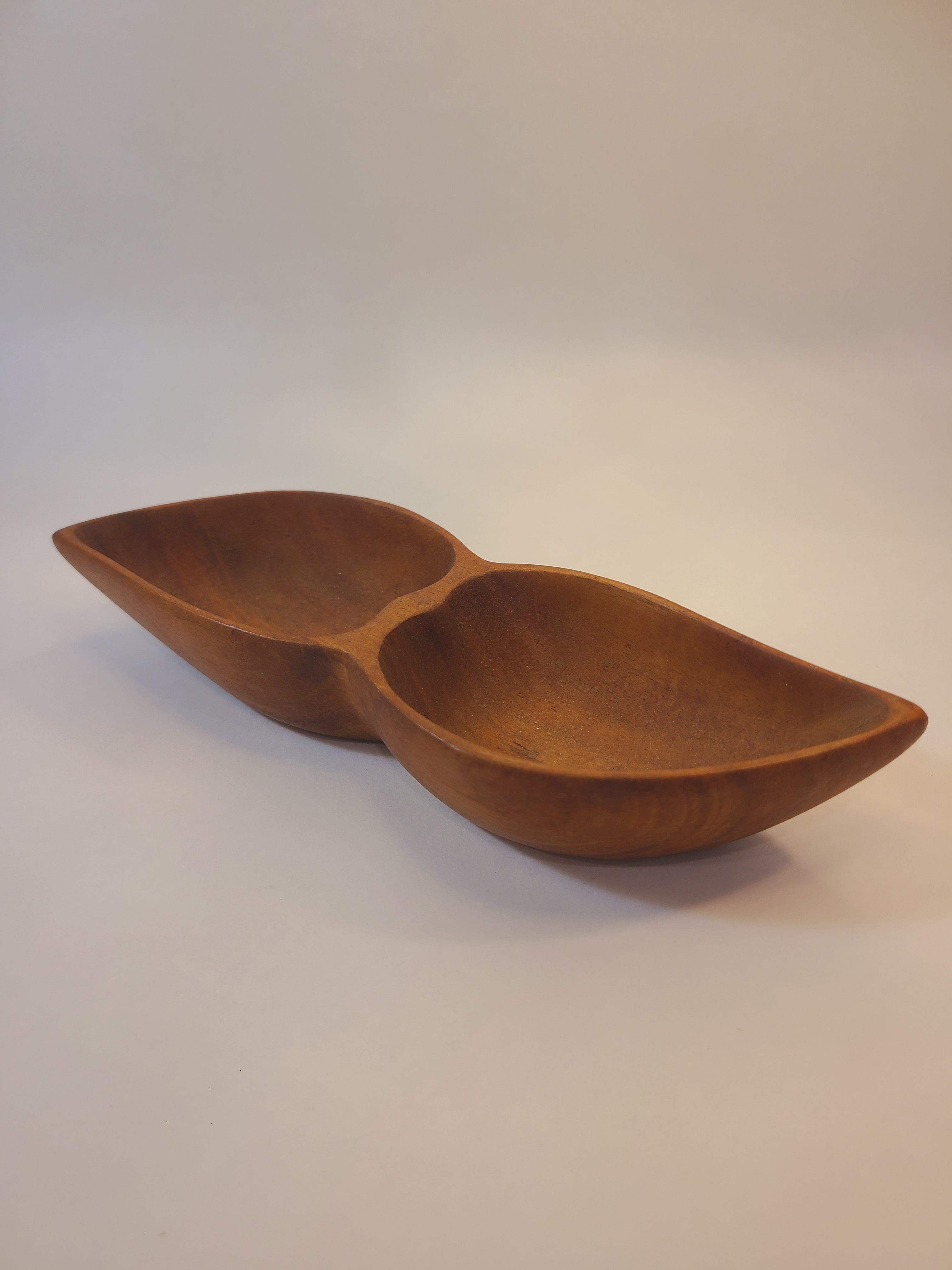 A vintage mid-century wooden bowl with a sculptural, leaf shape, shown against a plain off-white wall.