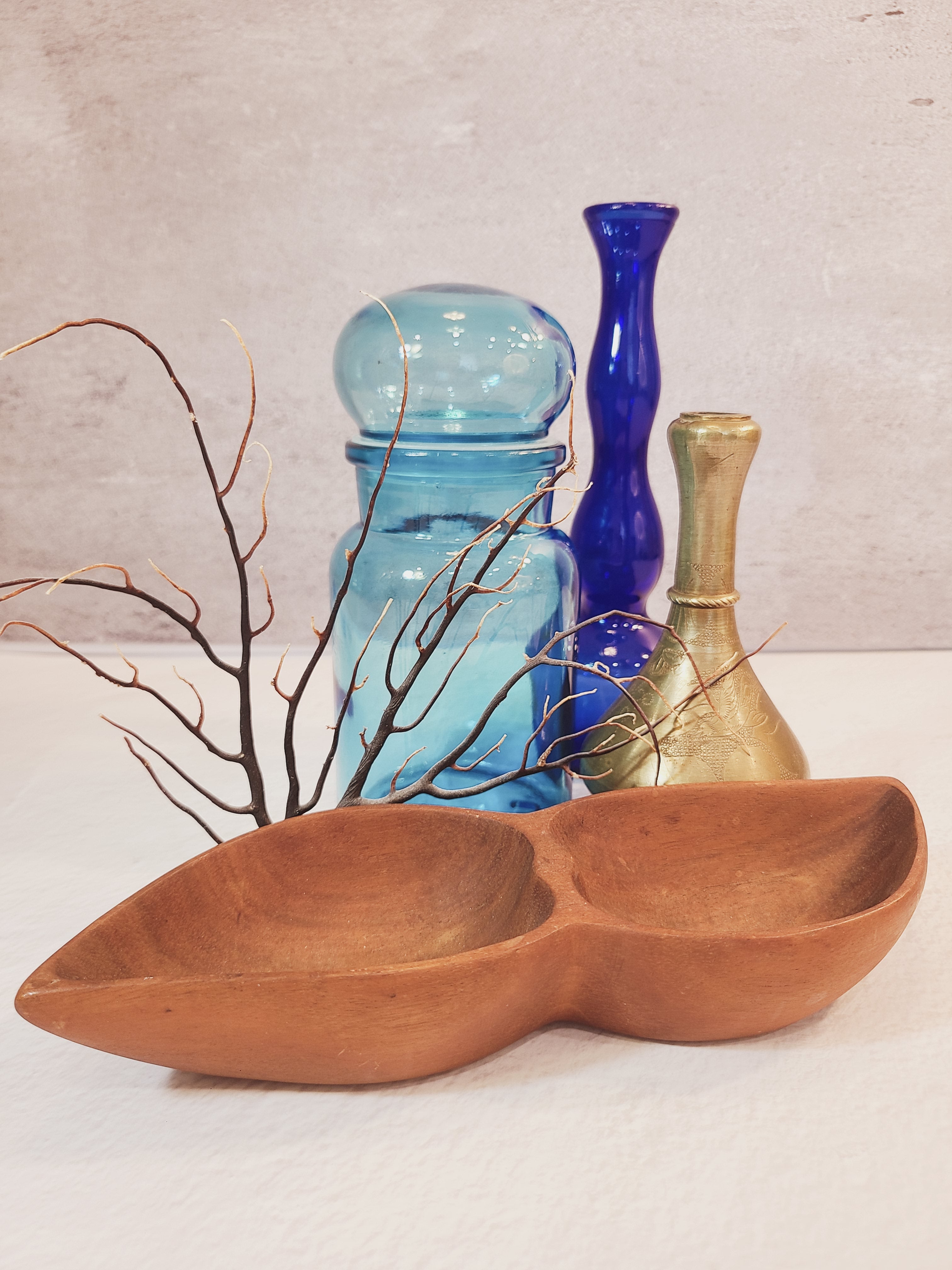 Vintage mid-century wood divided bowl in the foreground, styled with soft coral, brass vase, glass bud vase, and glass jar.
