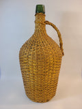 Vintage demijohn green glass with original rattan wrapping on plain background.