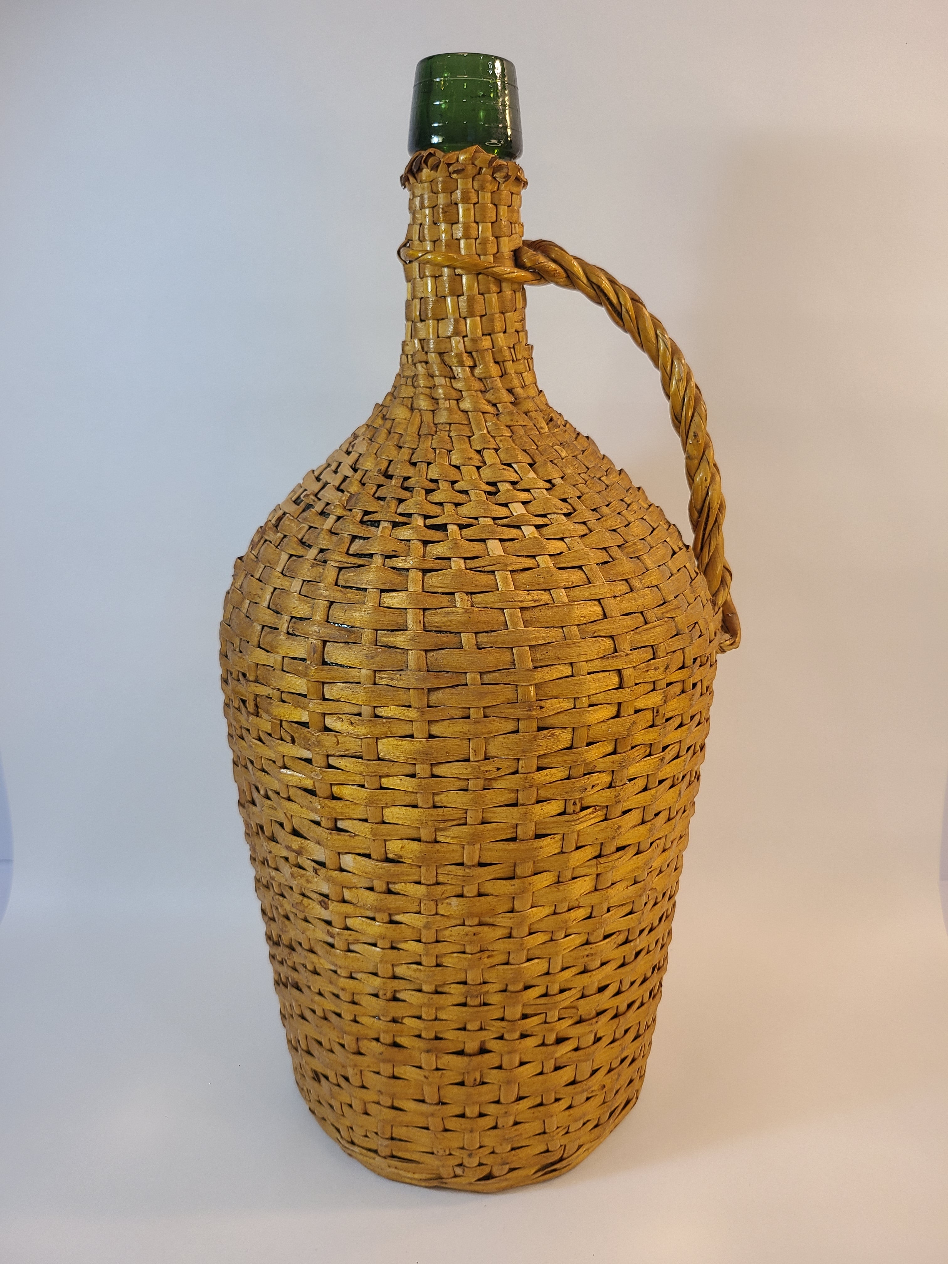 Vintage demijohn green glass with original rattan wrapping on plain background.
