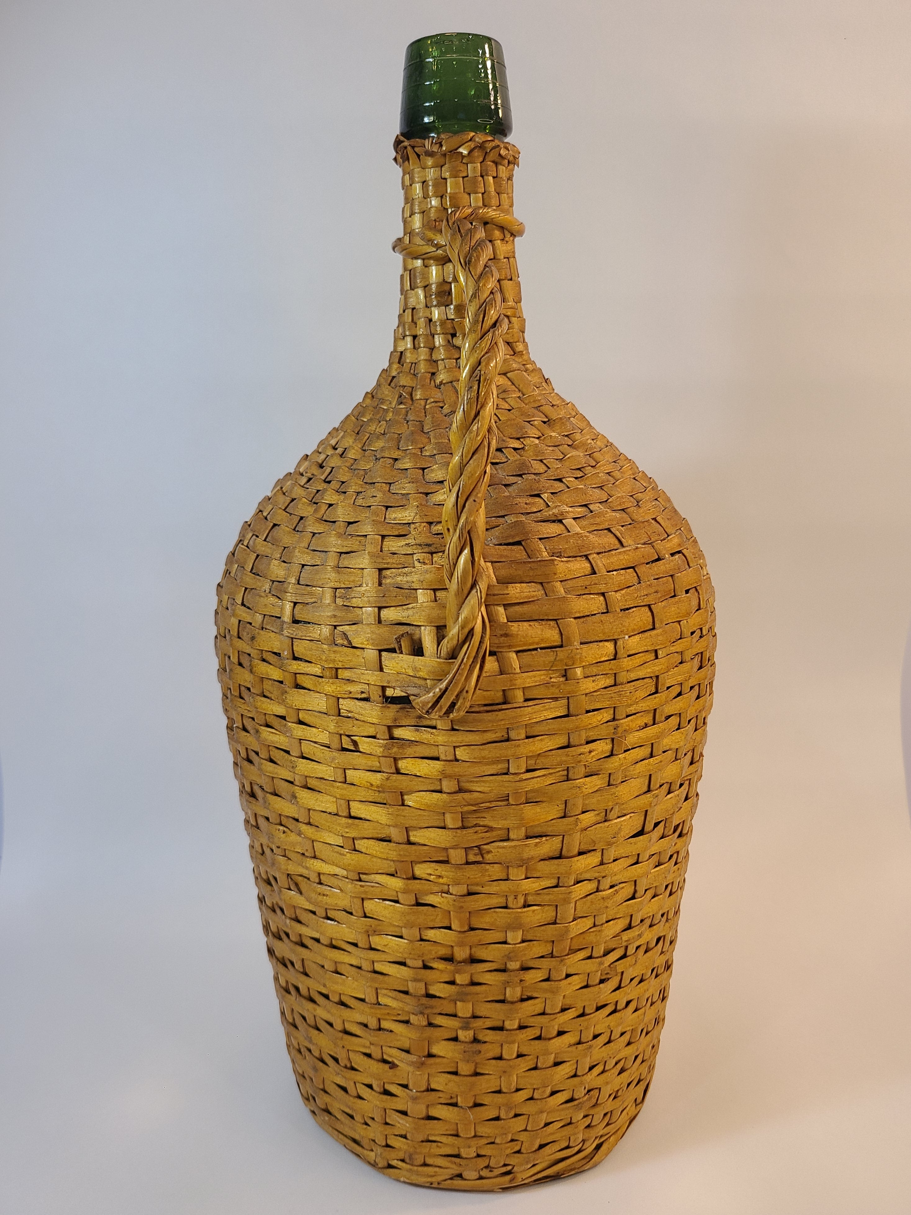 Vintage demijohn green glass with original rattan wrapping on plain background highlighting handle.