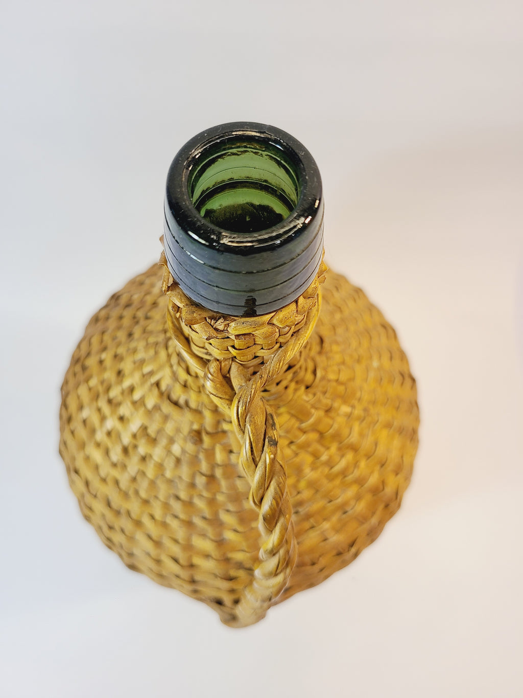 Top view of Vintage demijohn green glass with original rattan wrapping on plain background.