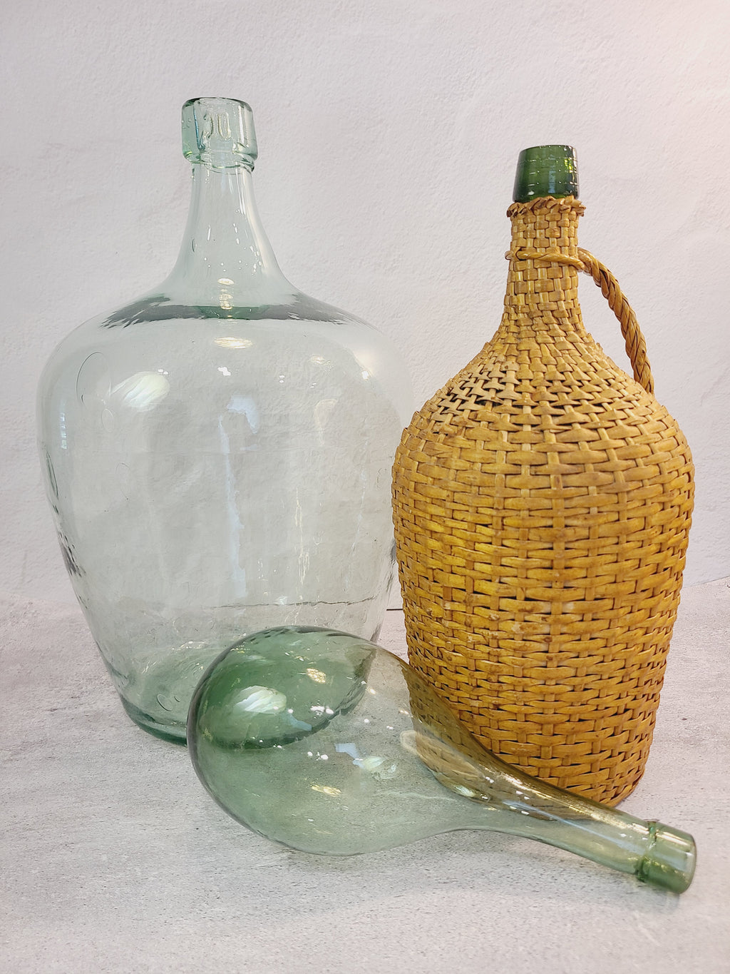Vintage demijohn green glass with original rattan wrapping displayed with other vintage bottles.