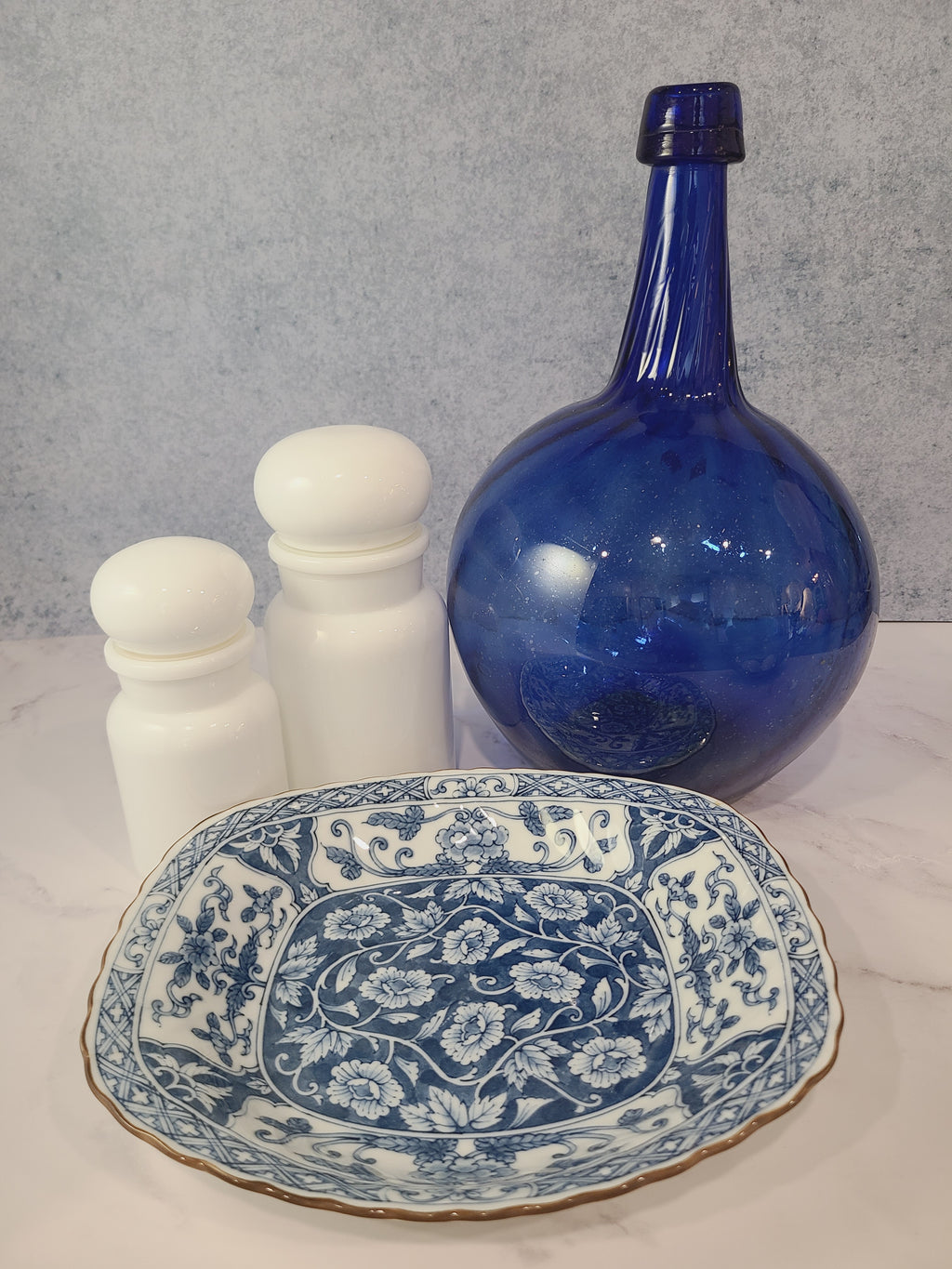 A vintage rectangular blue and white porcelain serving platter featuring an intricate floral and vine pattern made in Japan styled with blue bottle and white jars.
