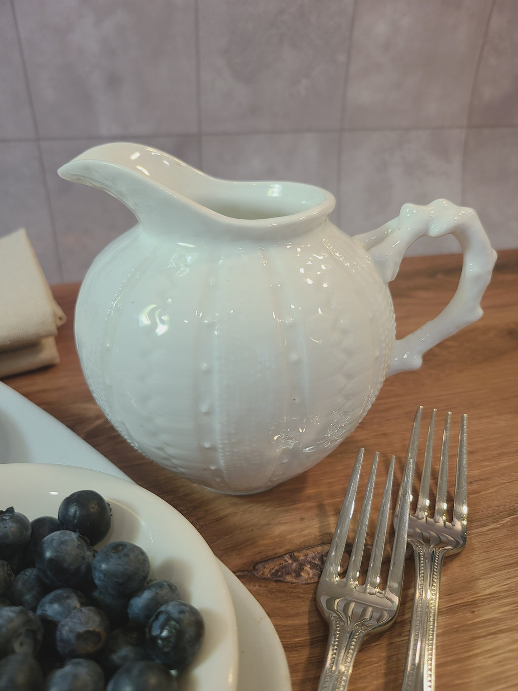 Close up of Vintage Paris Royal pitcher or creamer with sea urchin design displayed with blueberries in bowls, silverware, and linen napkins.