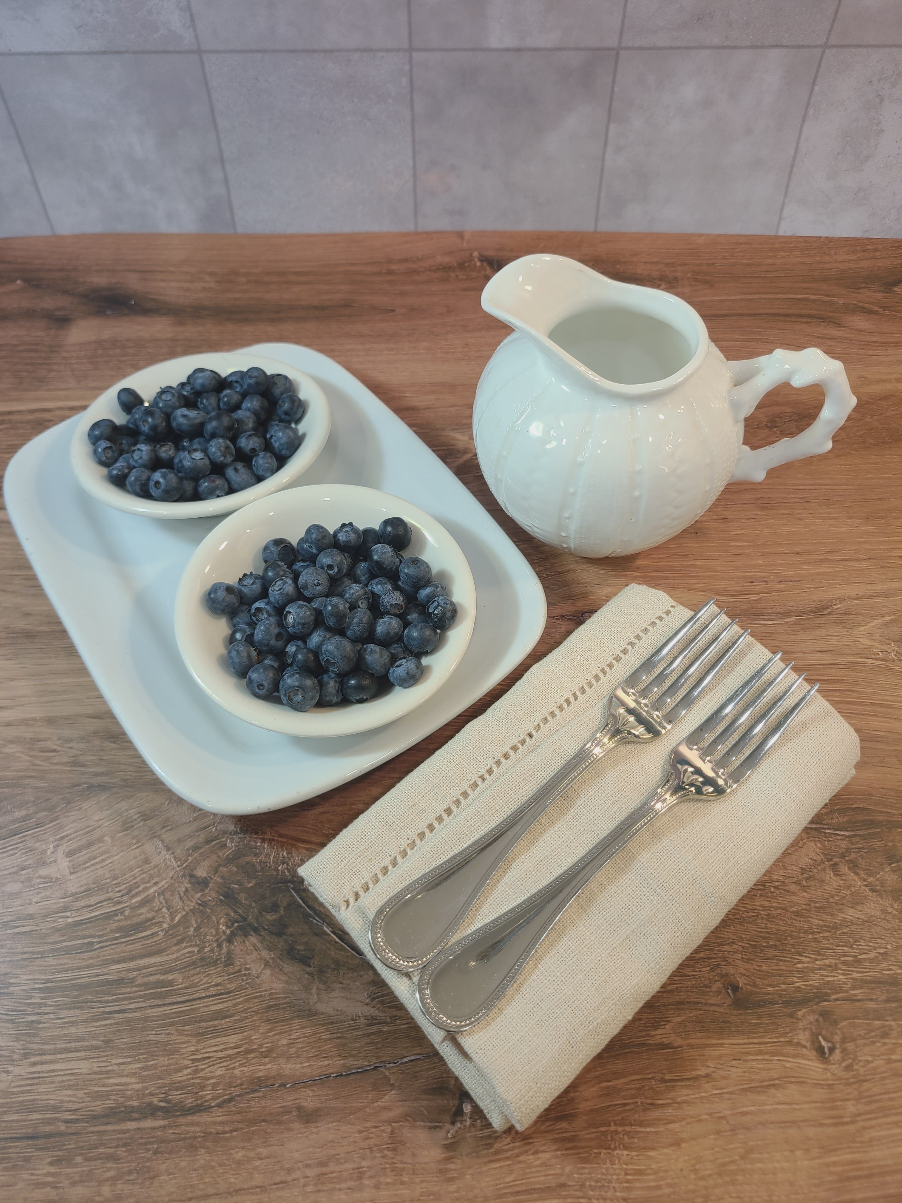 Vintage Paris Royal pitcher or creamer with sea urchin design displayed with blueberries in bowls, silverware, and linen napkins.