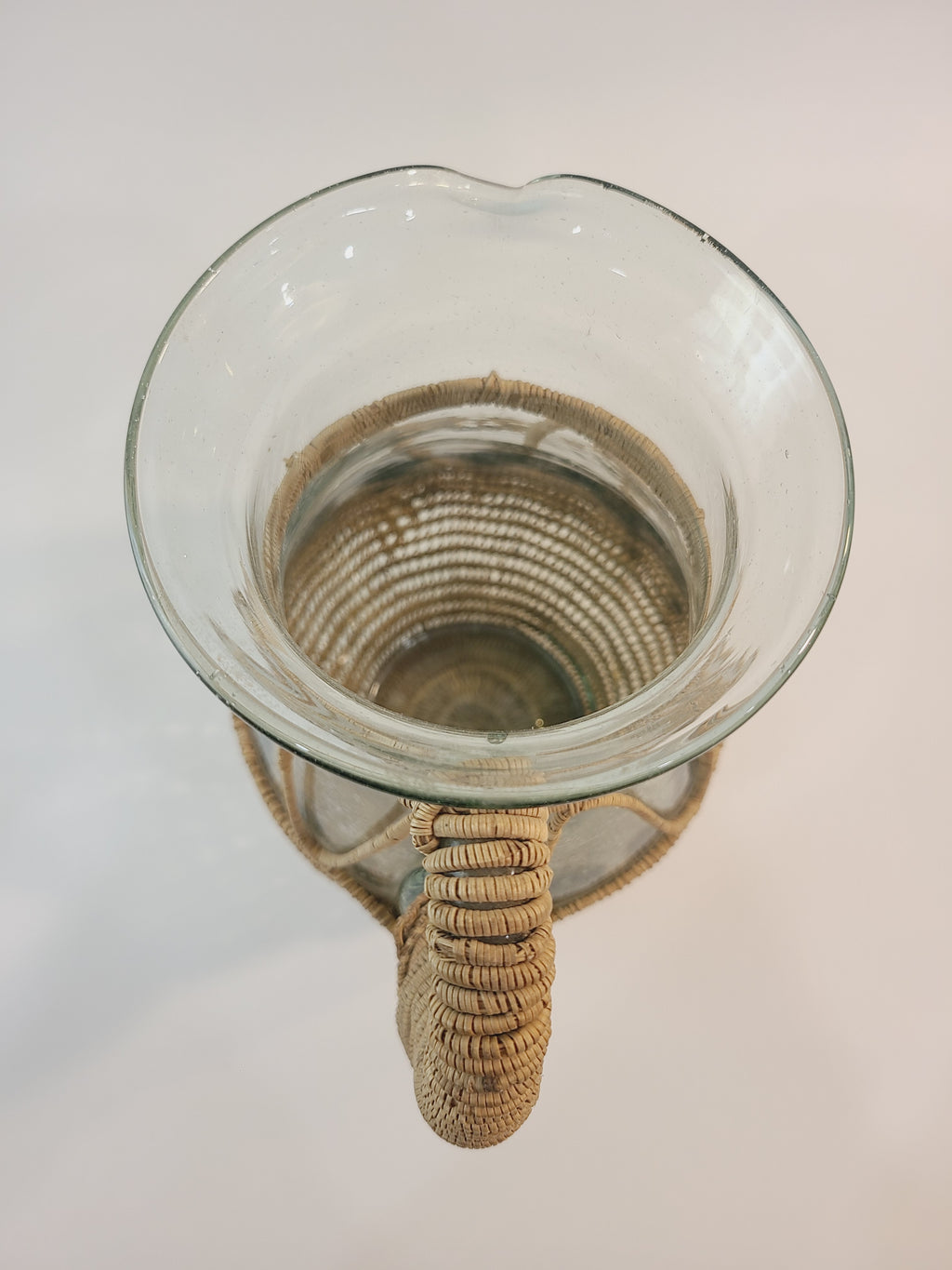 A vintage clear glass pitcher wrapped in a woven natural fiber shown from above.