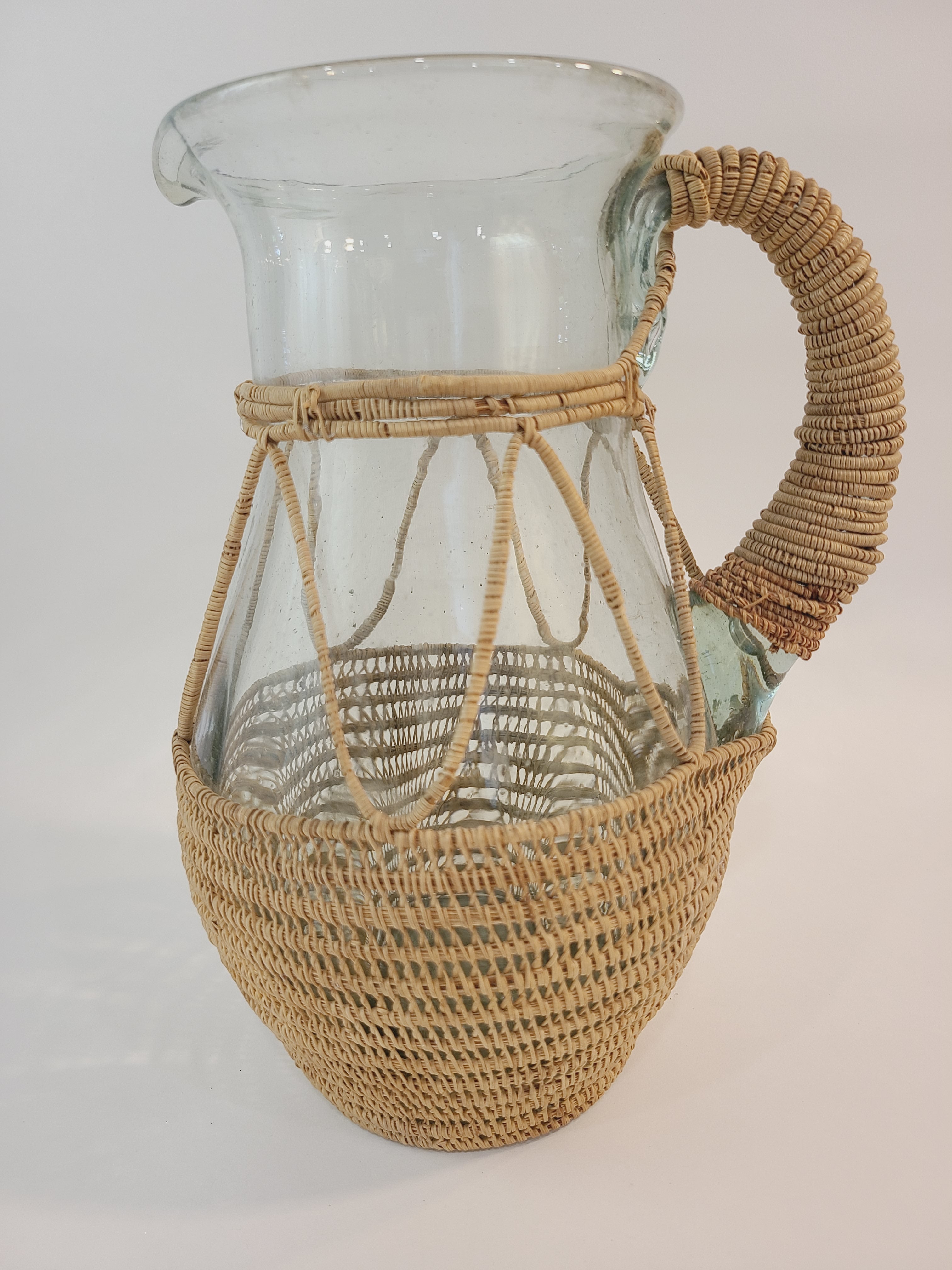 A vintage clear glass pitcher wrapped in a woven natural fiber from the side.