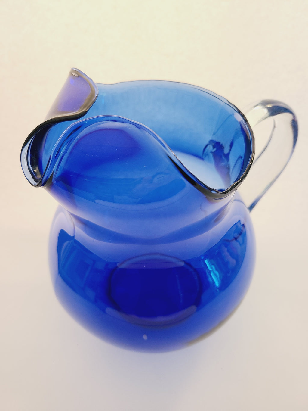 A vintage cobalt blue glass pitcher with a clear glass handle, shown from above