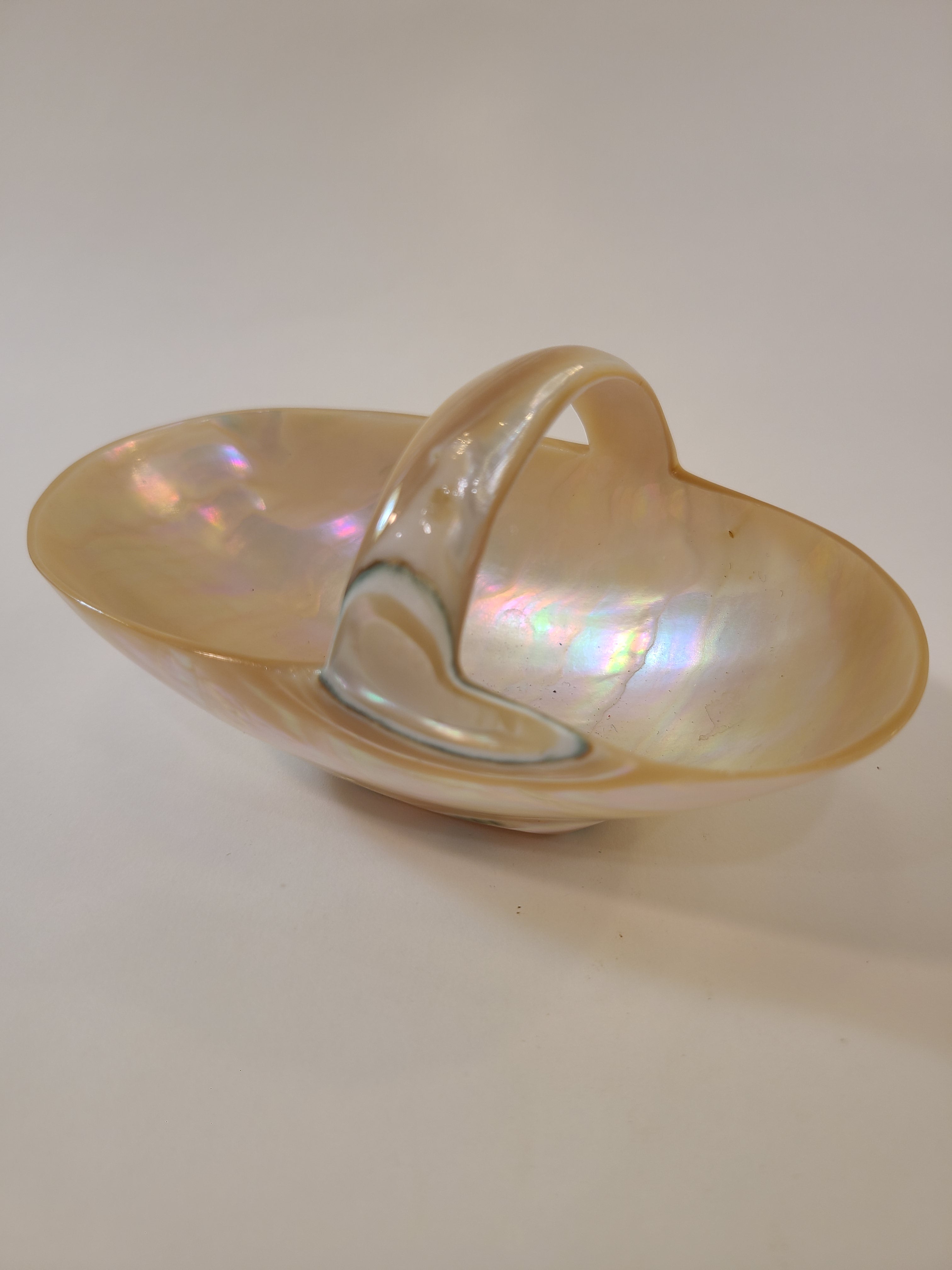 Basket carved from a shell showing mother of pearl glossy finish and subtle rainbow reflections, photographed against a plain light background.