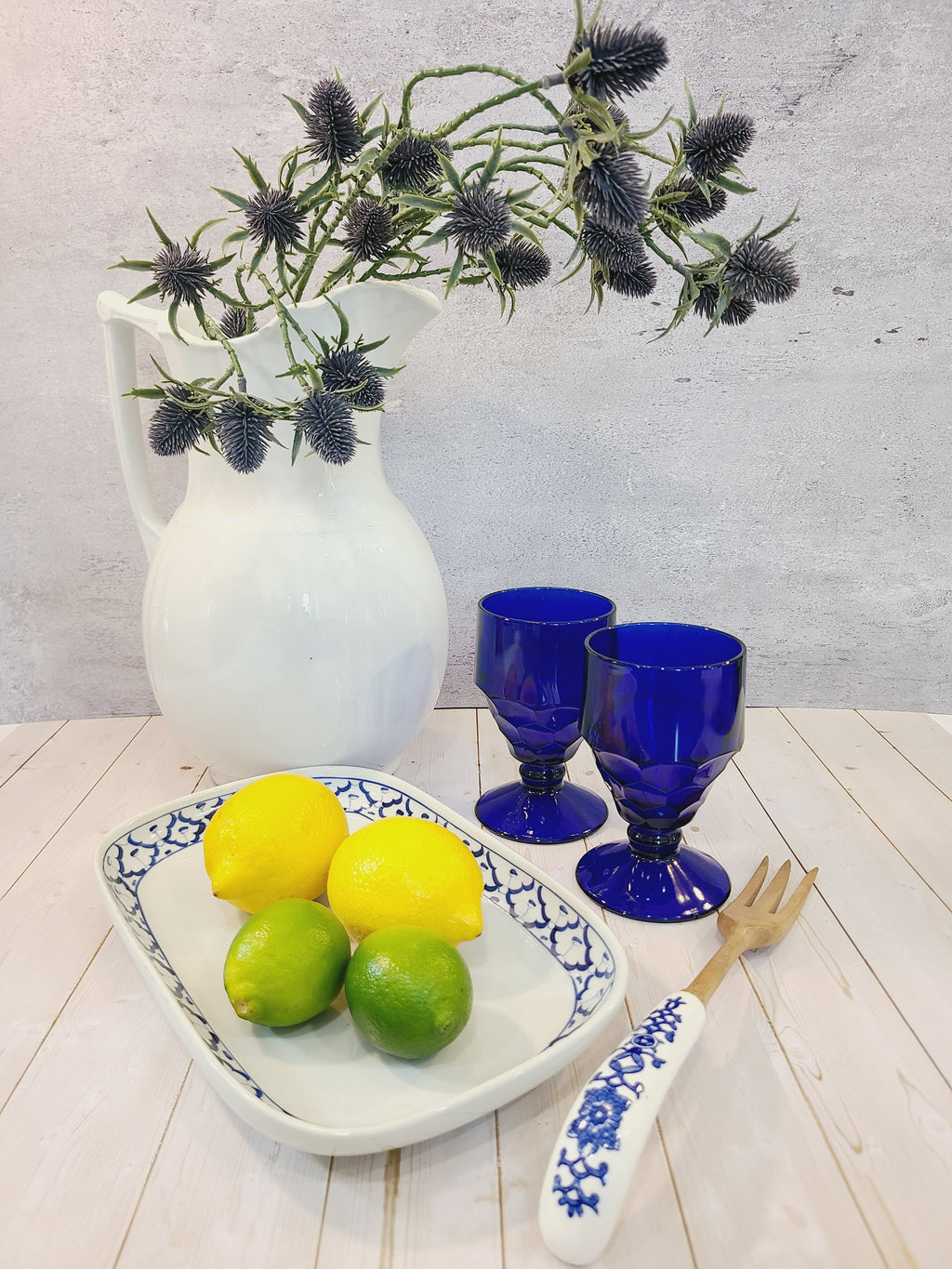 Antique white Alfred Meakin Royal Ironstone Pitcher styled with cobalt blue goblets, blue and white platter holding lemons, wooden fork with ceramic handle.